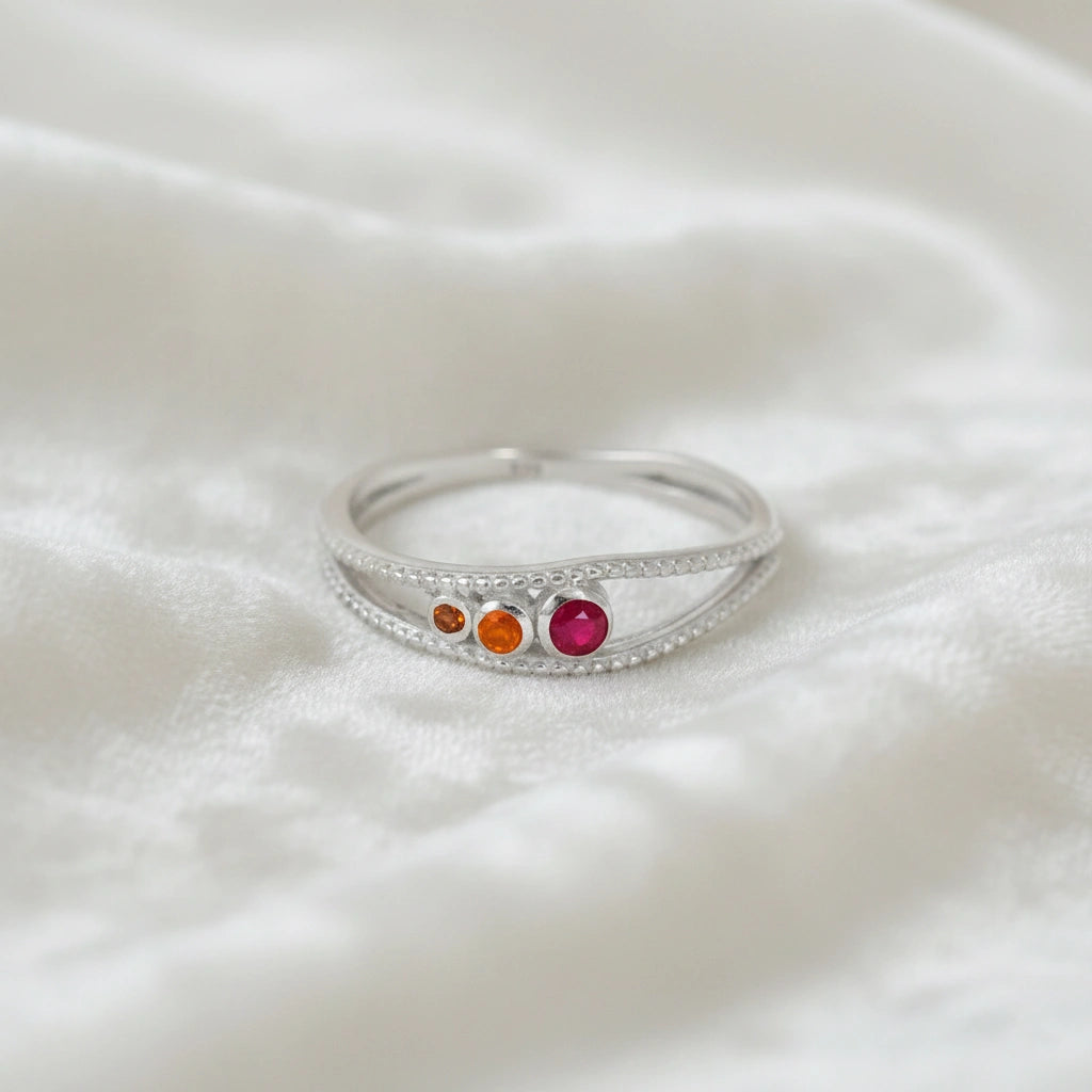 Three-stone-ring-in-sterling-silver-with-pink-red-and-orange-stones-in-front-view-on-soft-white-fabric-background