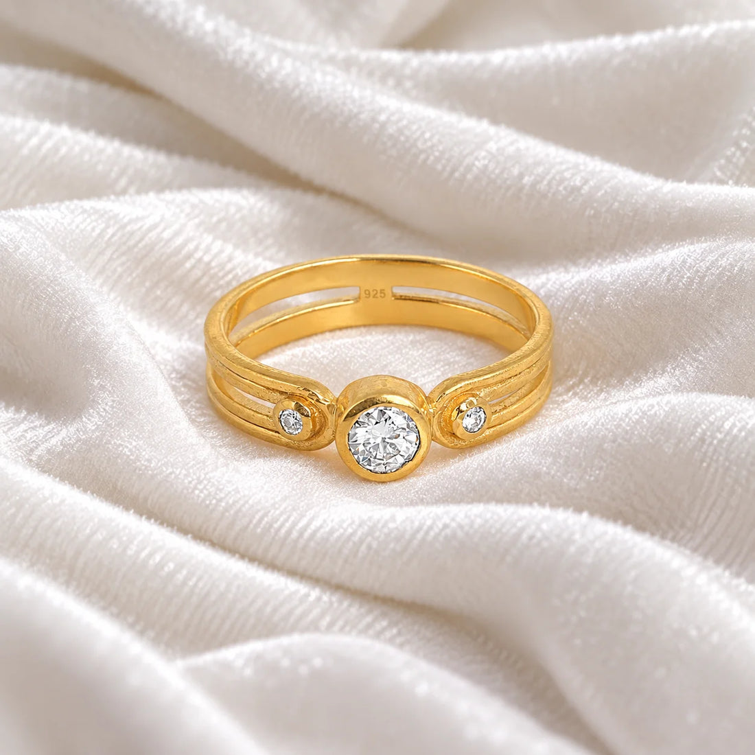 Three_stone_ring_in_gold_plated_silver_with_round_lab_grown_diamonds_at_front_angle_view_on_soft_fabric_background