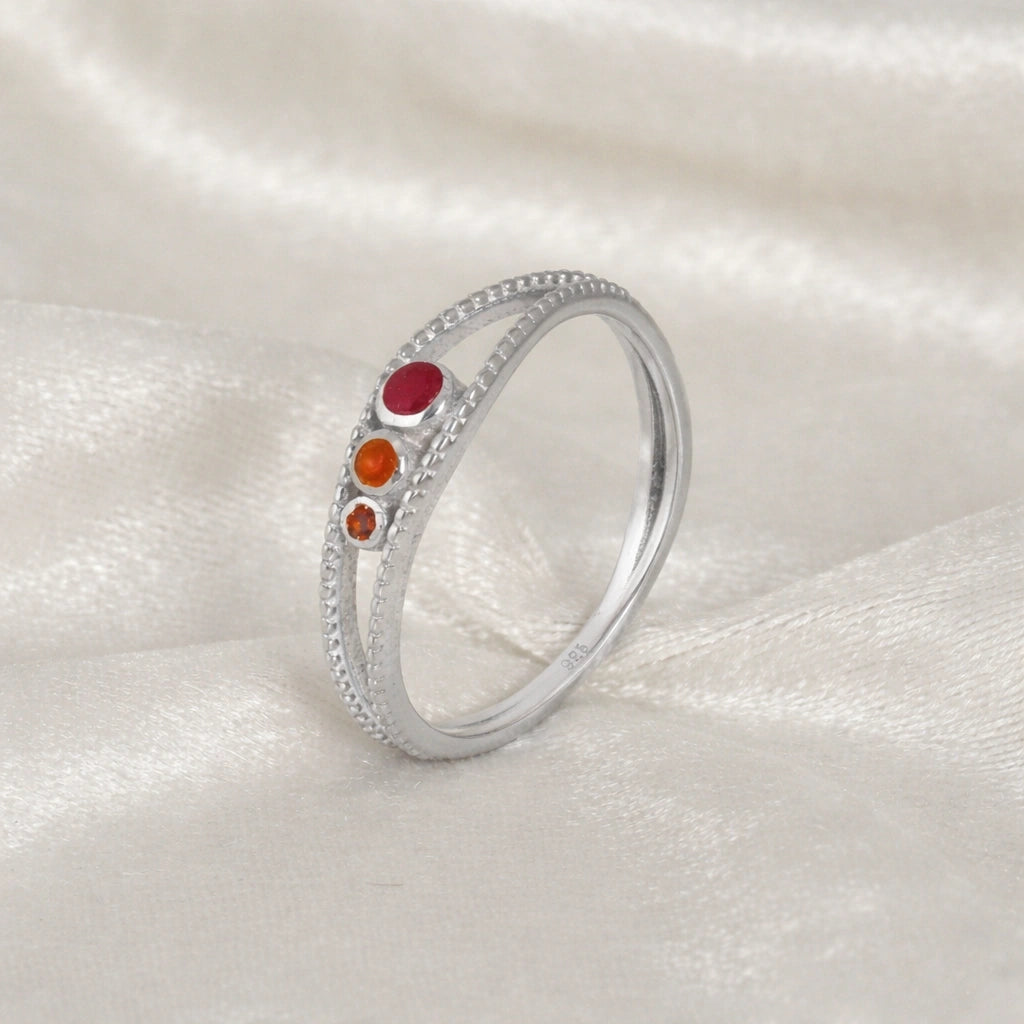 Three-stone-ring-in-sterling-silver-with-pink-red-and-orange-stones-in-angled-side-view-on-soft-white-fabric-background