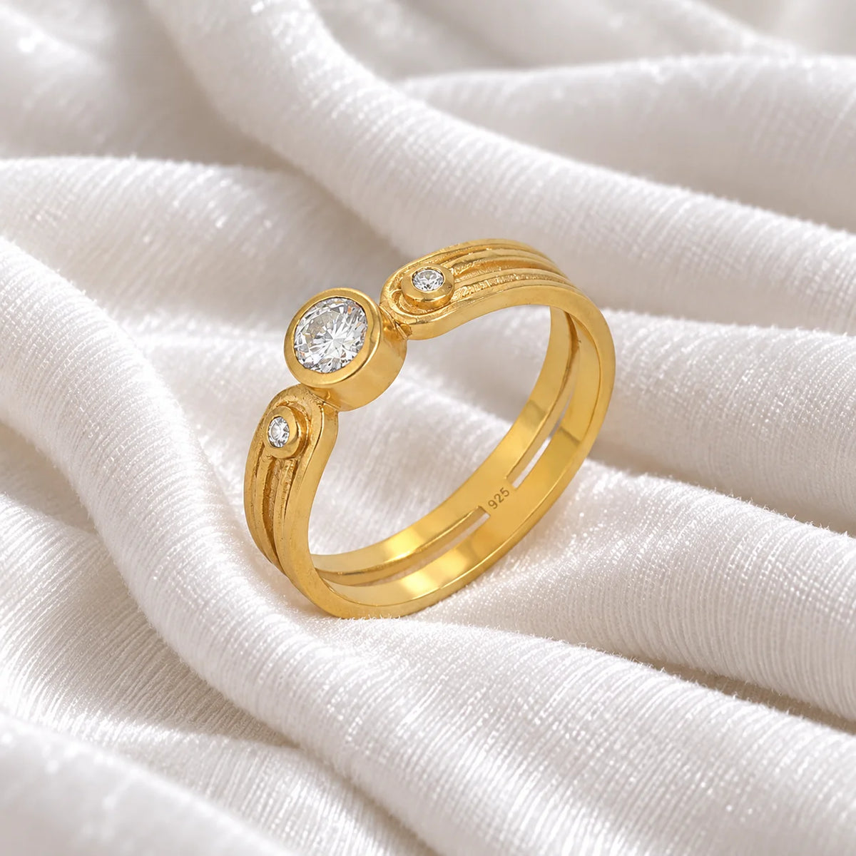 Three_stone_ring_in_gold_plated_silver_with_round_lab_grown_diamonds_at_side_angle_view_on_soft_fabric_background