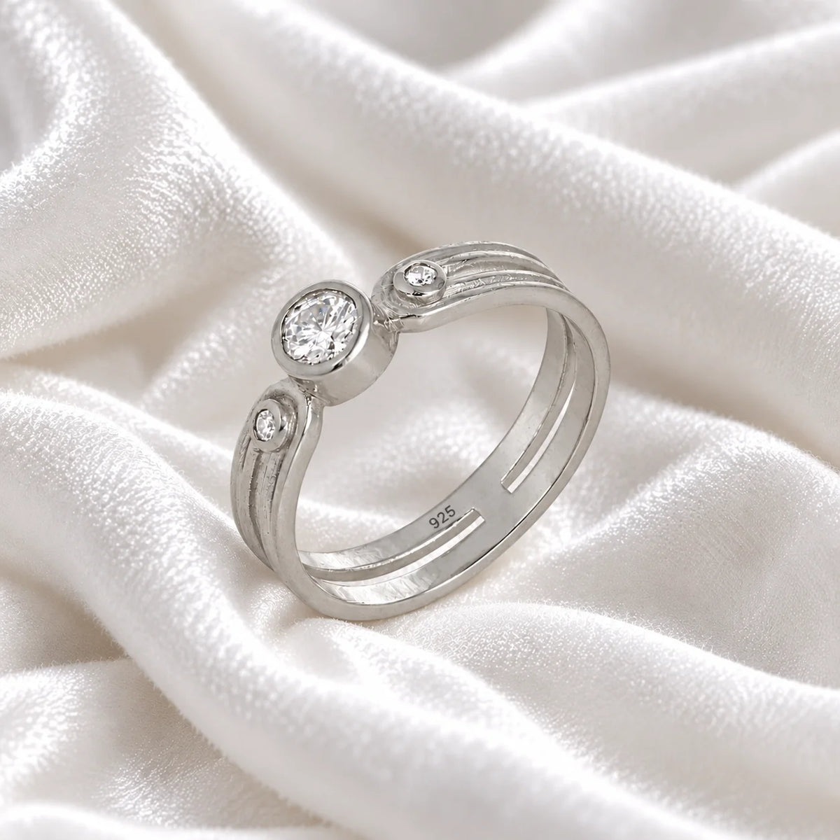 Three_stone_ring_in_sterling_silver_with_round_lab_grown_diamonds_at_side_angle_view_on_soft_fabric_background