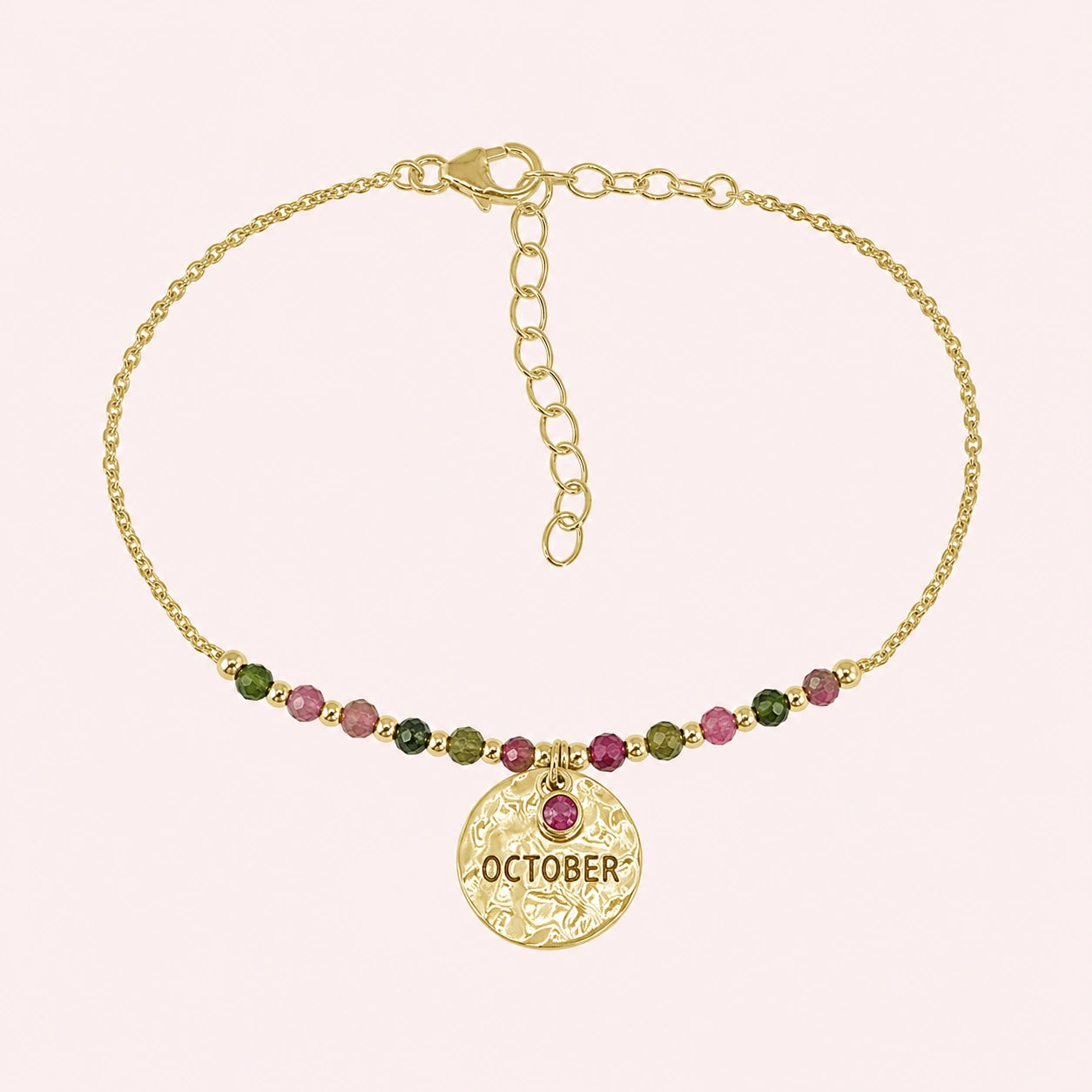 Birthstone_bracelet_in_gold_plated_silver_with_October_charm_and_tourmaline_beads_on_fine_chain_on_solid_pink_background