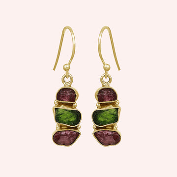 Trending_earrings_in_gold_plated_silver_with_three_raw_tourmaline_stones_at_front_angle_view_on_solid_pink_background