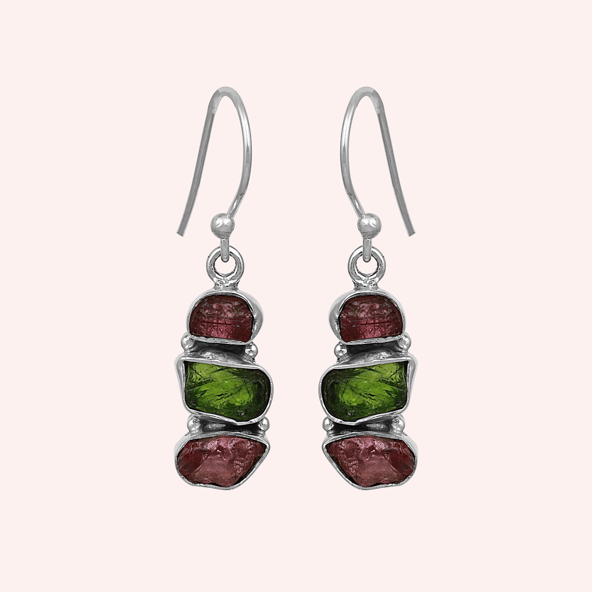 Trending_earrings_in_sterling_silver_with_three_raw_tourmaline_stones_at_front_angle_view_on_solid_pink_background