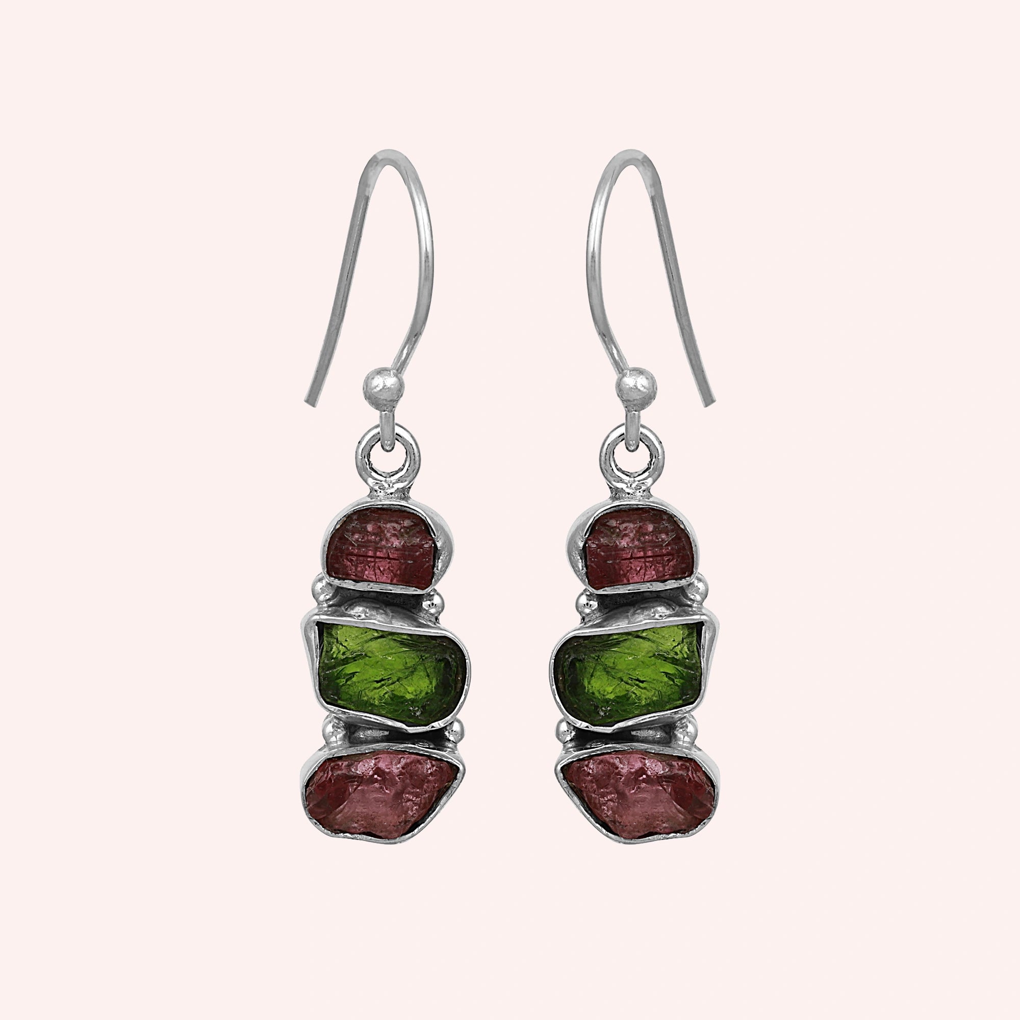 Trending_earrings_in_sterling_silver_with_three_raw_tourmaline_stones_at_front_angle_view_on_solid_pink_background