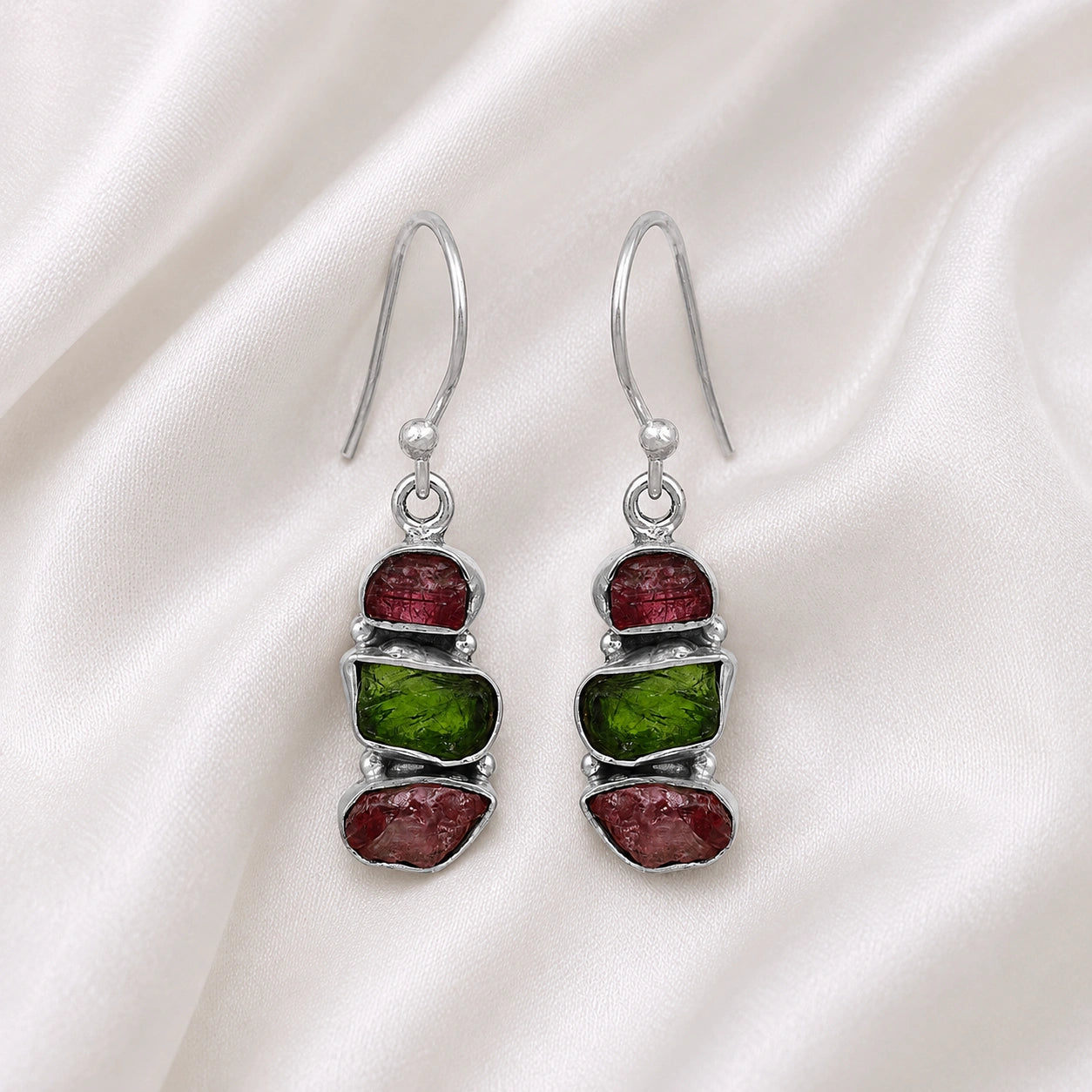 Trending_earrings_in_sterling_silver_with_three_raw_tourmaline_stones_at_front_angle_view_on_soft_fabric_background