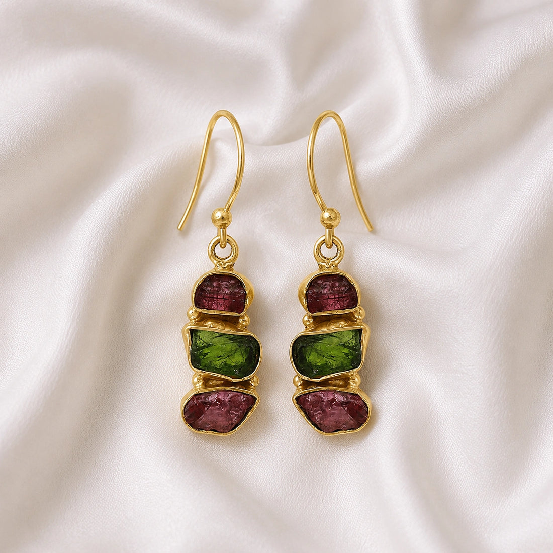 Trending_earrings_in_gold_plated_silver_with_three_raw_tourmaline_stones_at_front_angle_view_on_soft_fabric_background