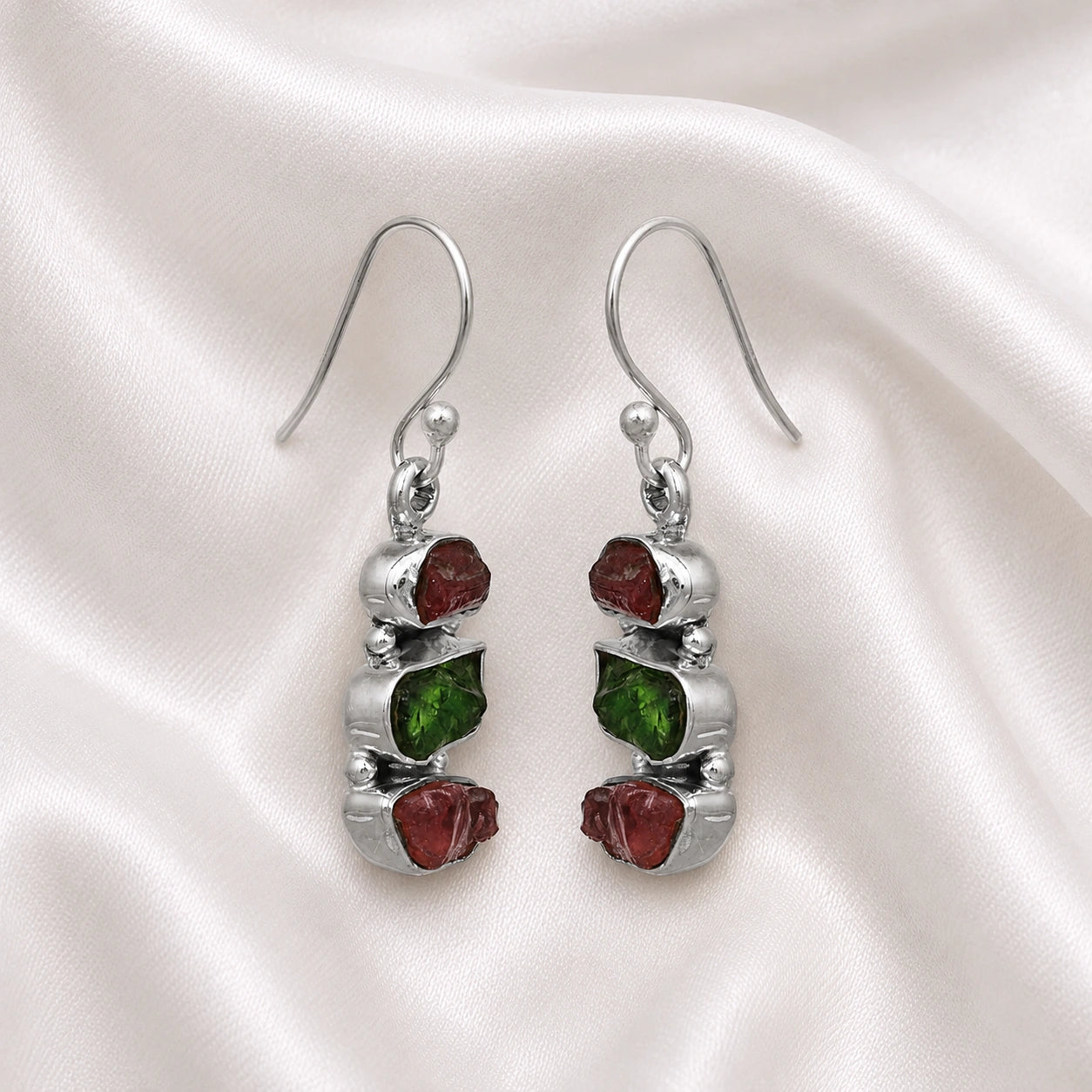 Trending_earrings_in_sterling_silver_with_three_raw_tourmaline_stones_at_slight_angle_view_on_soft_fabric_background