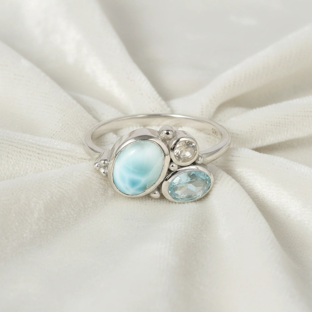 Detailed blue stone ring with Larimar Blue Topaz Moonstone resting on an off white draped fabric background viewed straight on