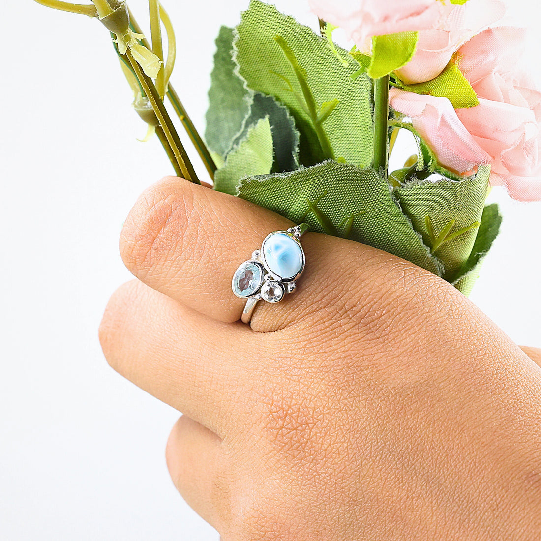 Detailed blue stone ring with Larimar Blue Topaz Moonstone resting on an off white draped fabric background viewed straight on
