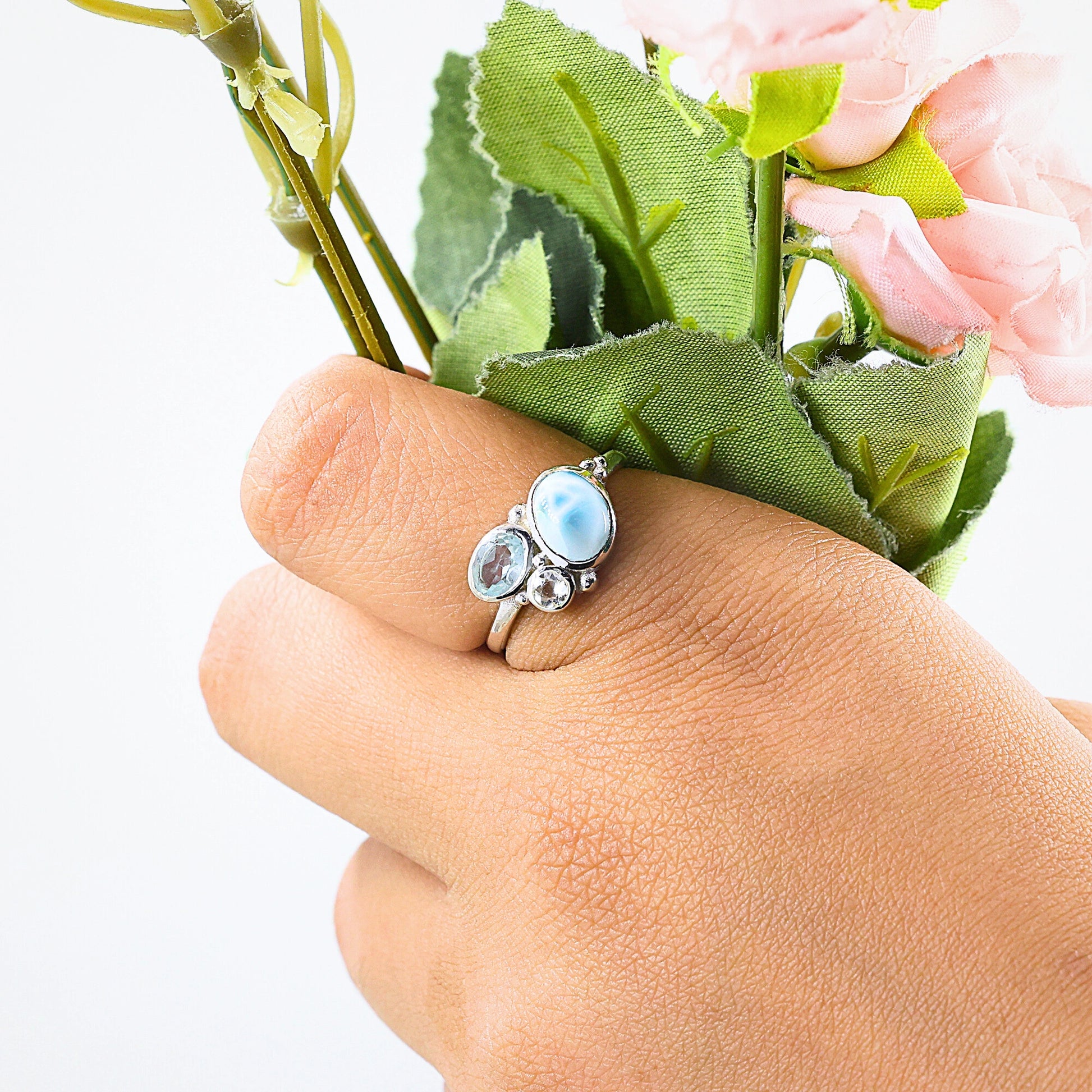 Blue stone ring with Larimar Blue Topaz Moonstone worn on a hand holding flowers against a white background viewed straight on