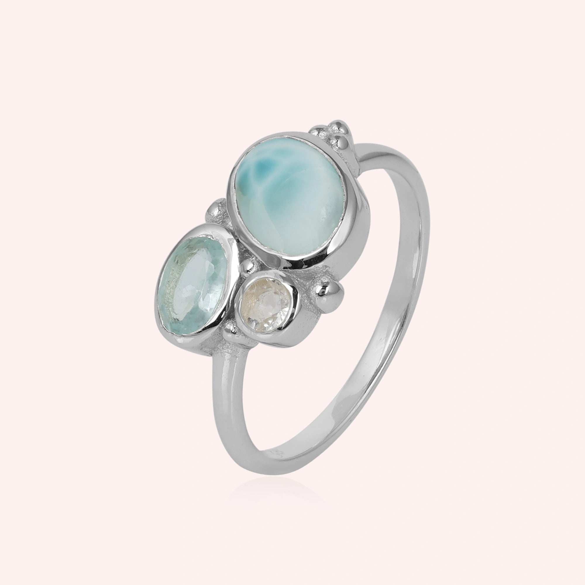 Shot of a beautiful blue stone ring featuring Larimar Blue Topaz and Moonstone on a light pink background viewed from an angle