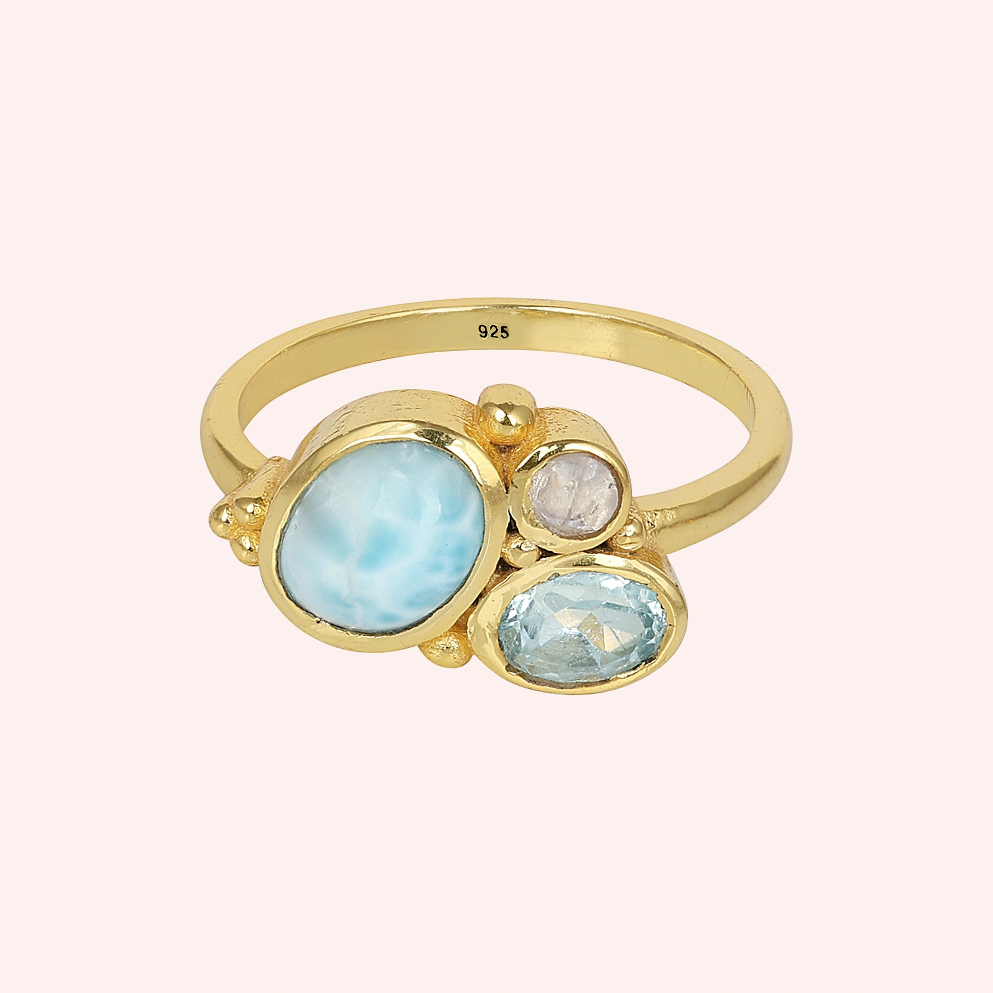 Shot of a beautiful blue stone ring gold plated with Larimar Blue Topaz Moonstone on a light pink background viewed straight on