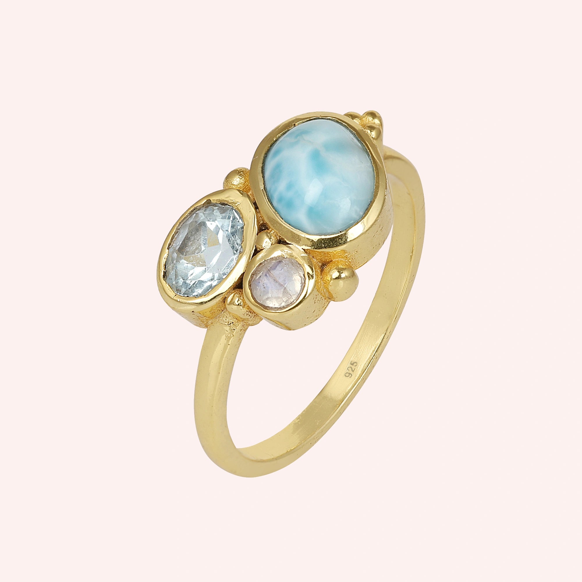 Shot of a beautiful blue stone ring gold plated with Larimar Blue Topaz Moonstone on a light pink background viewed from an angle