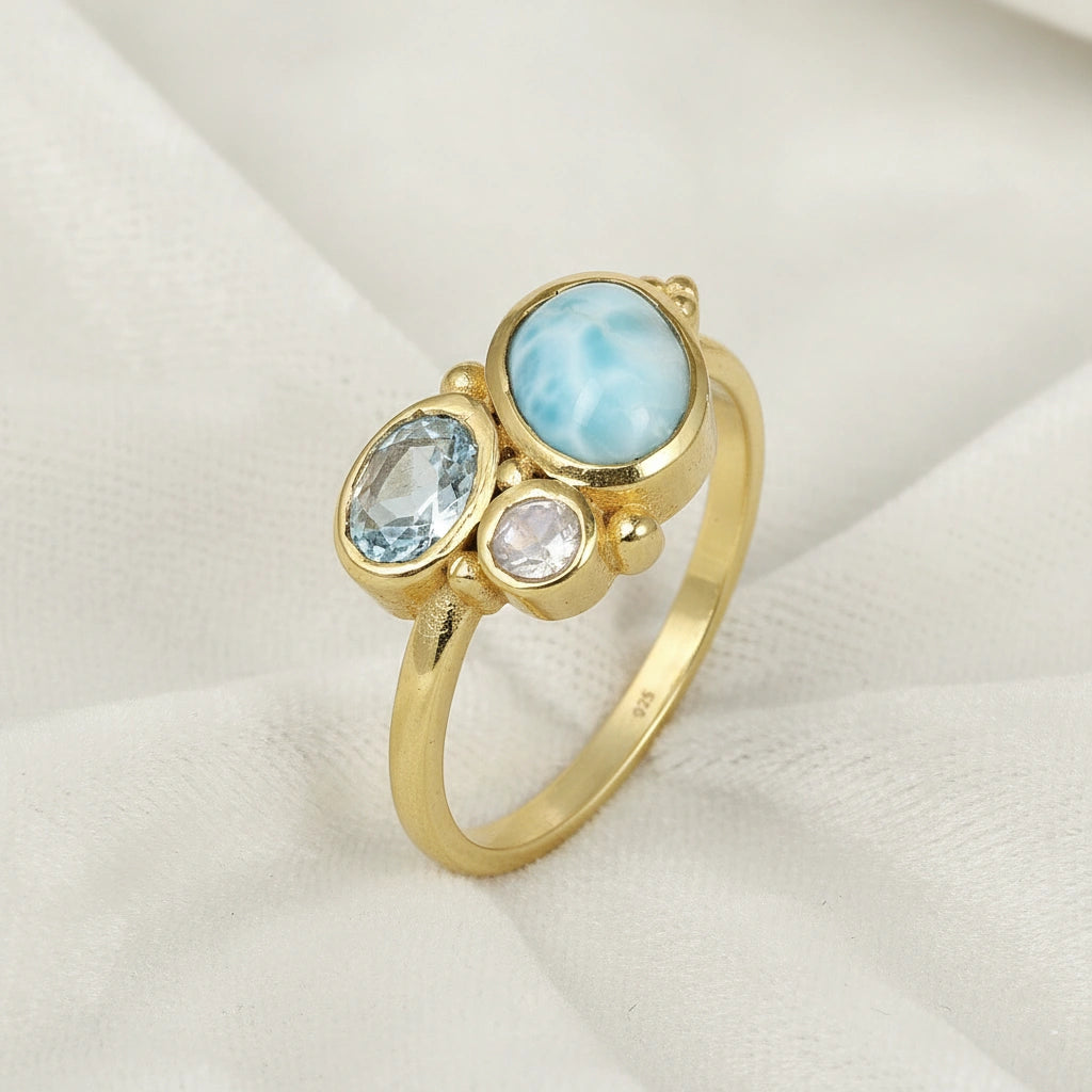 Detailed blue stone ring gold plated with Larimar Blue Topaz Moonstone on a soft white fabric background viewed from an angle