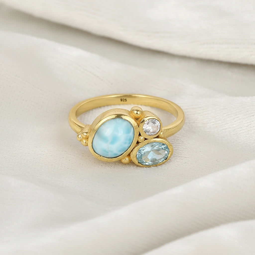 Detailed blue stone ring gold plated with Larimar Blue Topaz Moonstone on a soft white fabric background viewed straight on