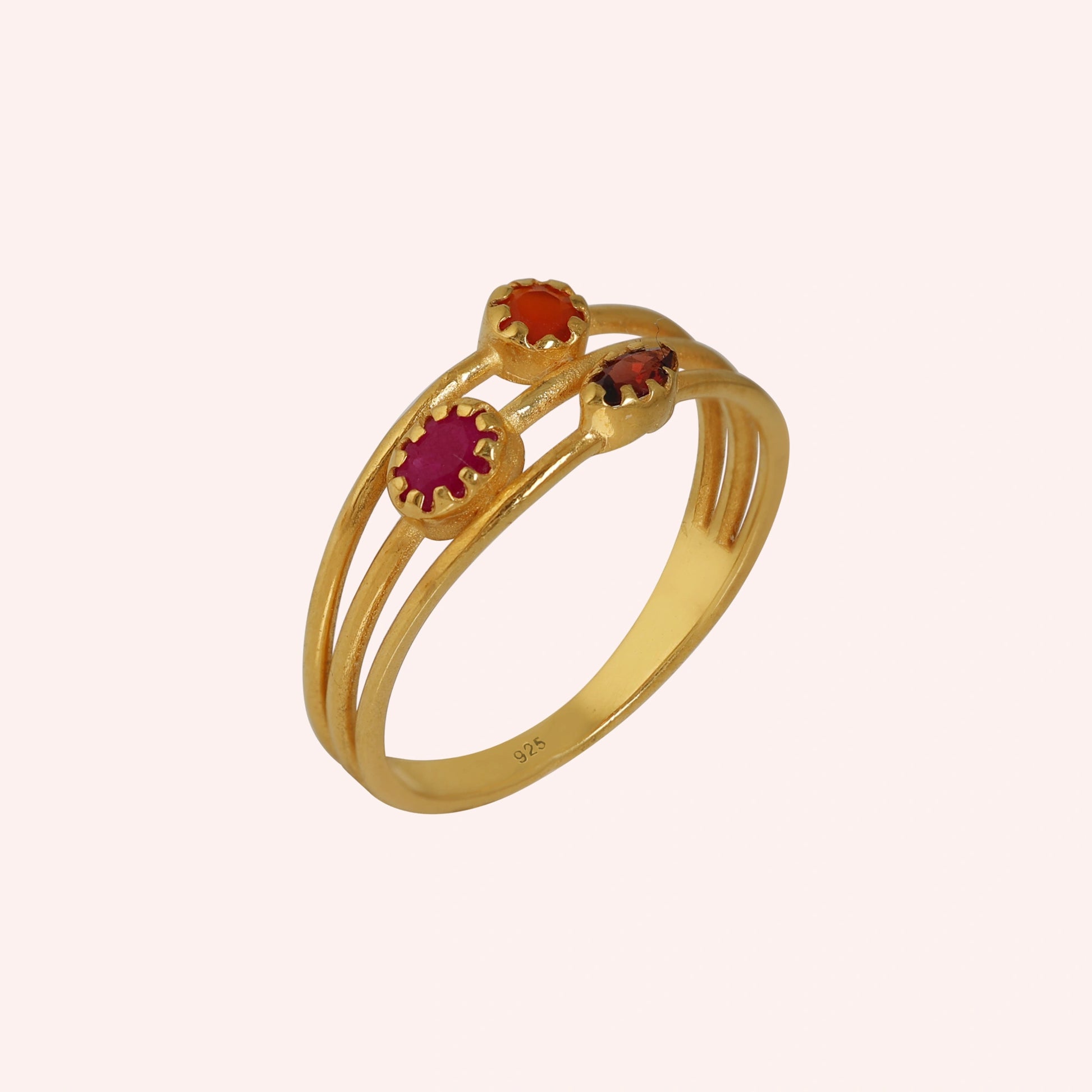 Triple-band-ring-with-ruby-carnelian-and-garnet-gemstones-in-gold-plated-silver-angled-view-on-soft-pink-background