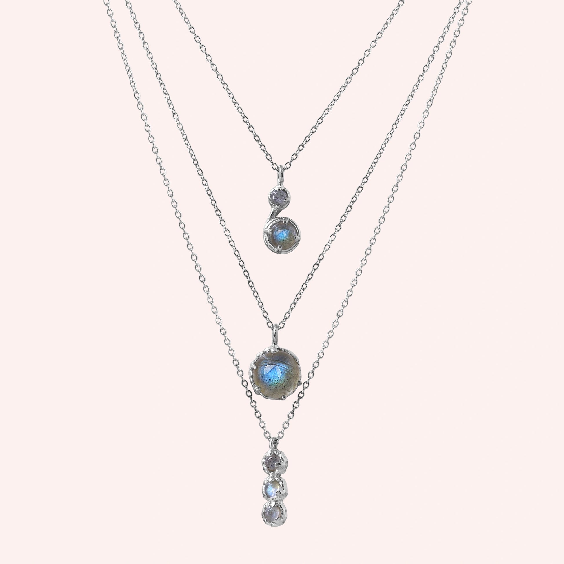 Labradorite necklace featuring three silver layers with blue flashing stones on a pale pink background straight on angle