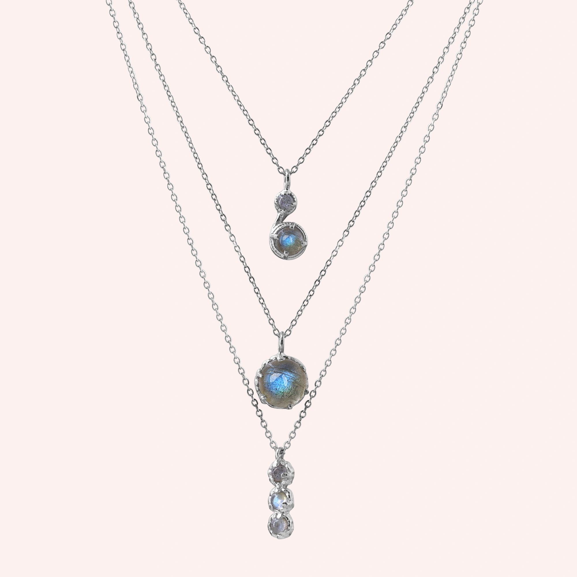 Labradorite necklace featuring three silver layers with blue flashing stones on a pale pink background straight on angle