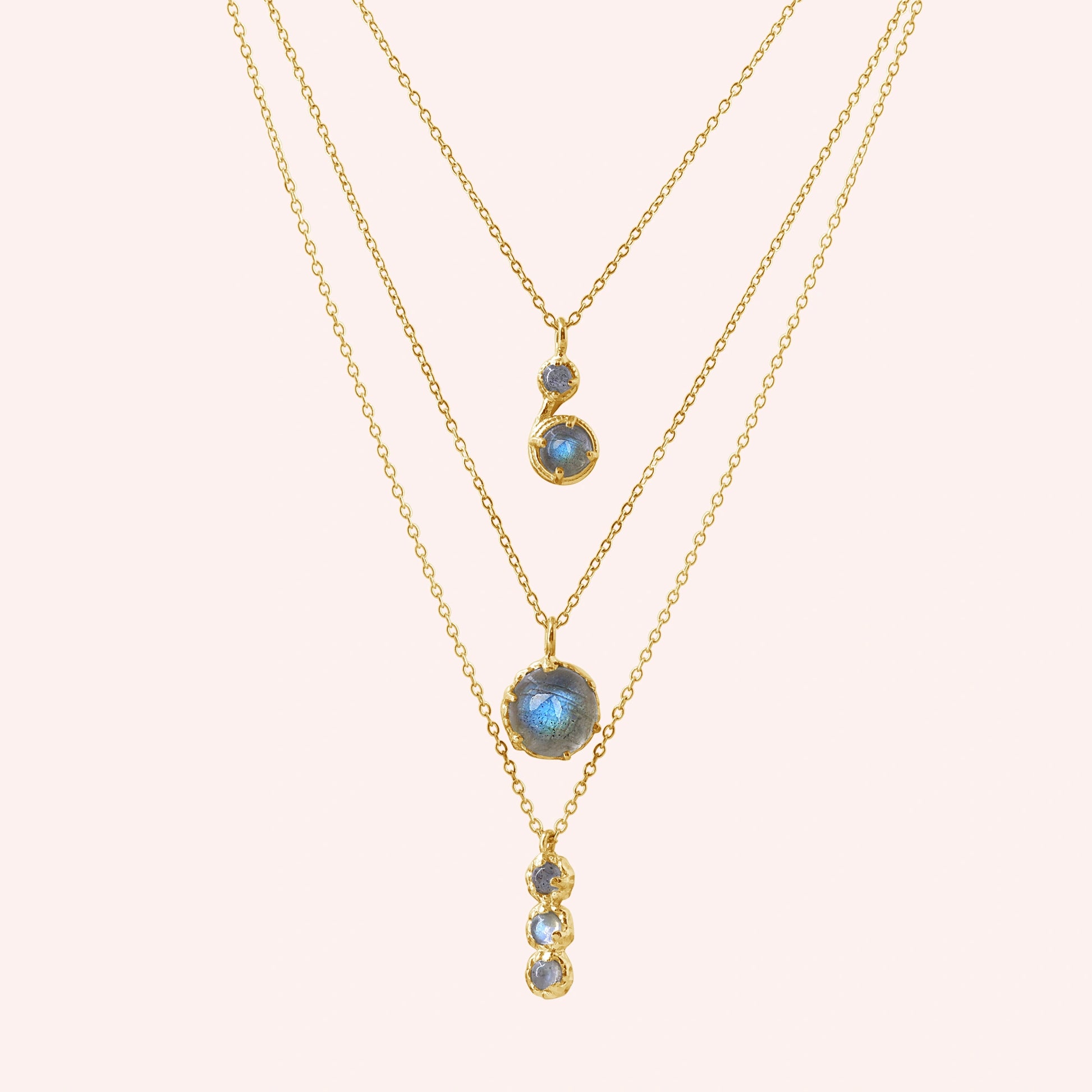 Labradorite necklace featuring three gold layers with blue flashing stones on a pale pink background at a straight on angle