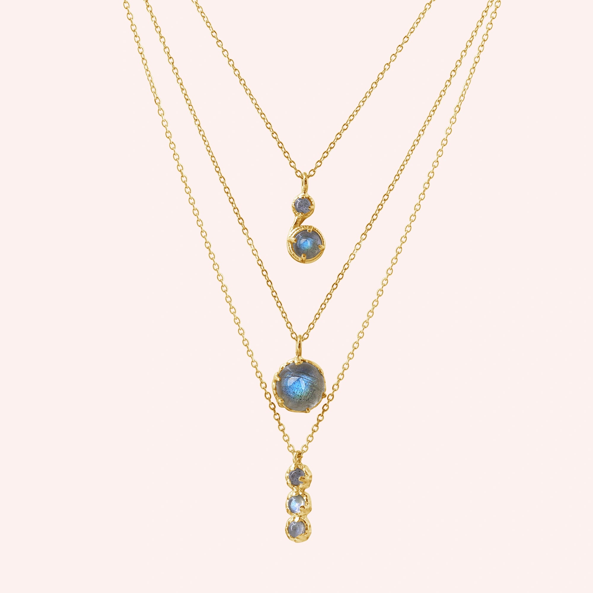 Labradorite necklace featuring three gold layers with blue flashing stones on a pale pink background at a straight on angle