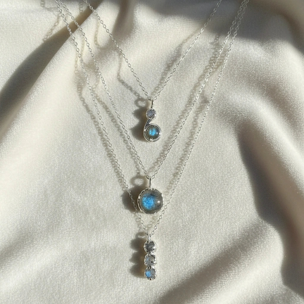 Labradorite necklace featuring three silver layers with blue flashing stones on an off white velvet cloth straight on angle