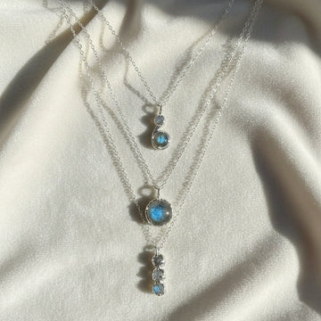 Labradorite necklace featuring three silver layers with blue flashing stones on an off white velvet cloth straight on angle