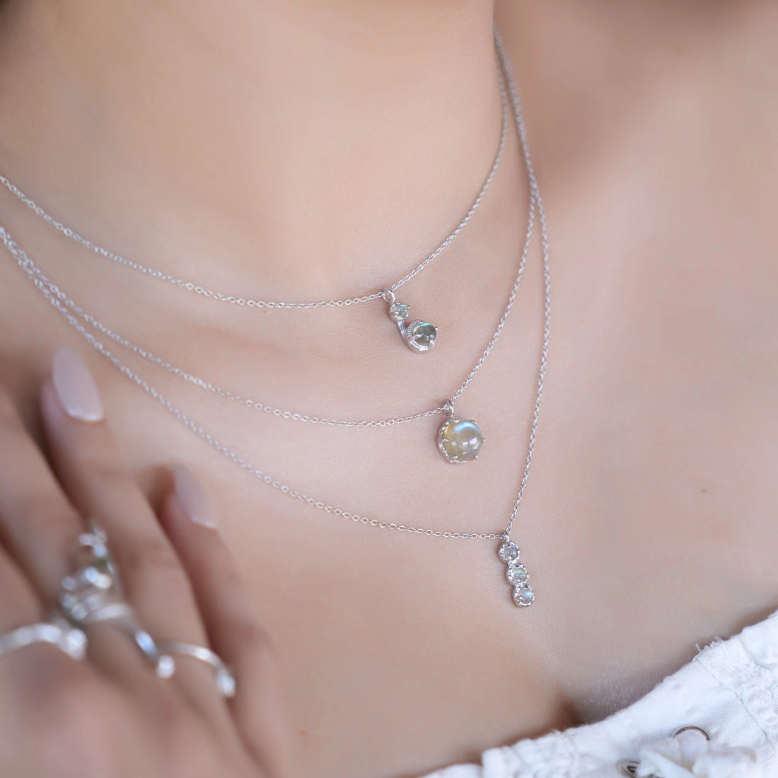 Labradorite necklace featuring three silver layers with blue flashing stones on an off white velvet cloth straight on angle