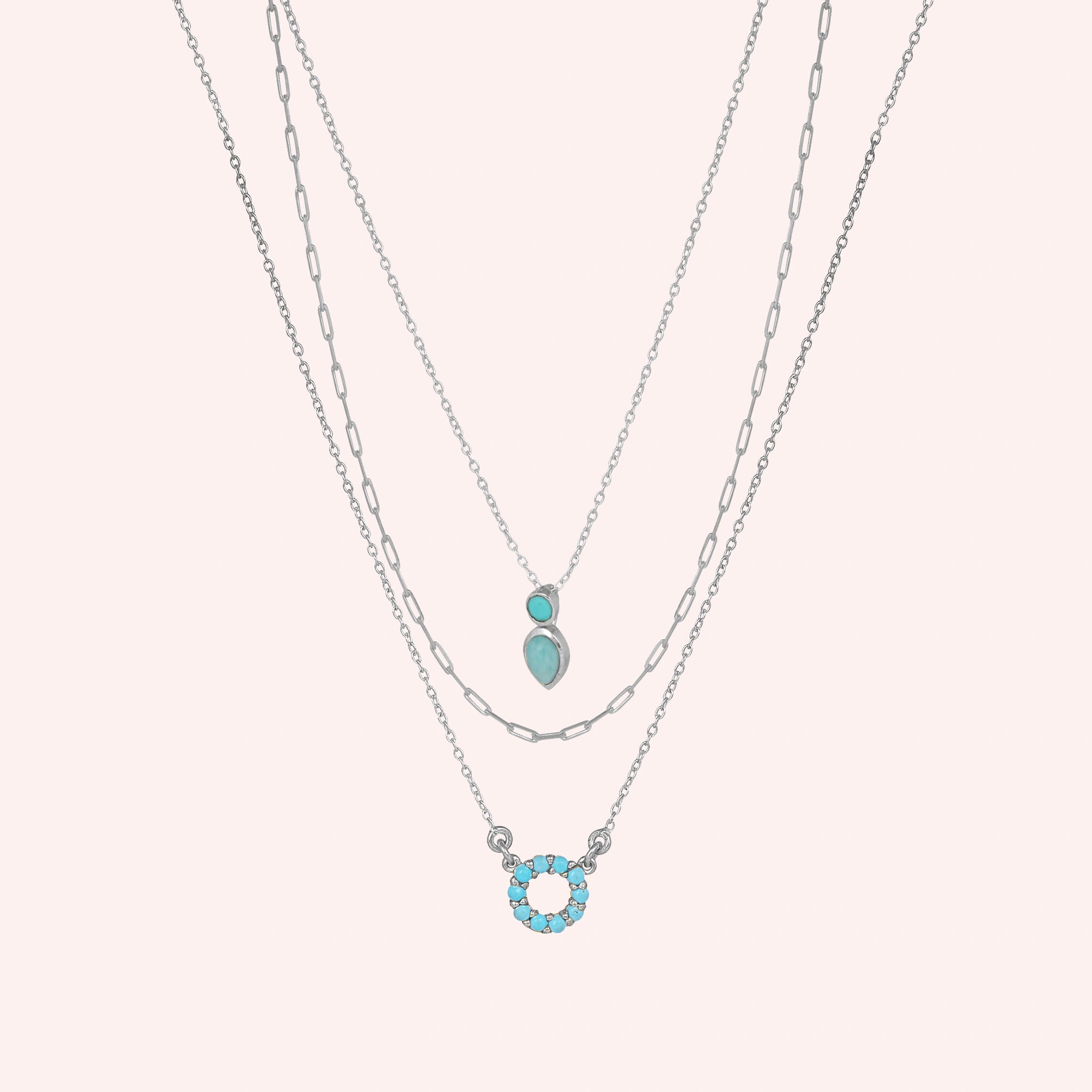 A front angle of three layered arizona turquoise necklace styles and a silver necklace for women over a light pink background