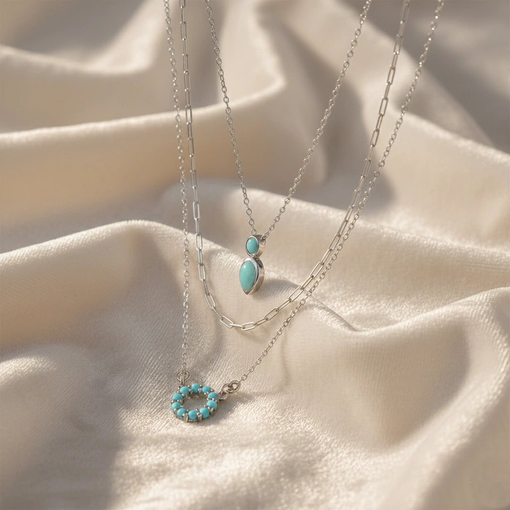 A front angle of gold plated arizona turquoise necklace sets and a silver necklace for women over a white fabric background