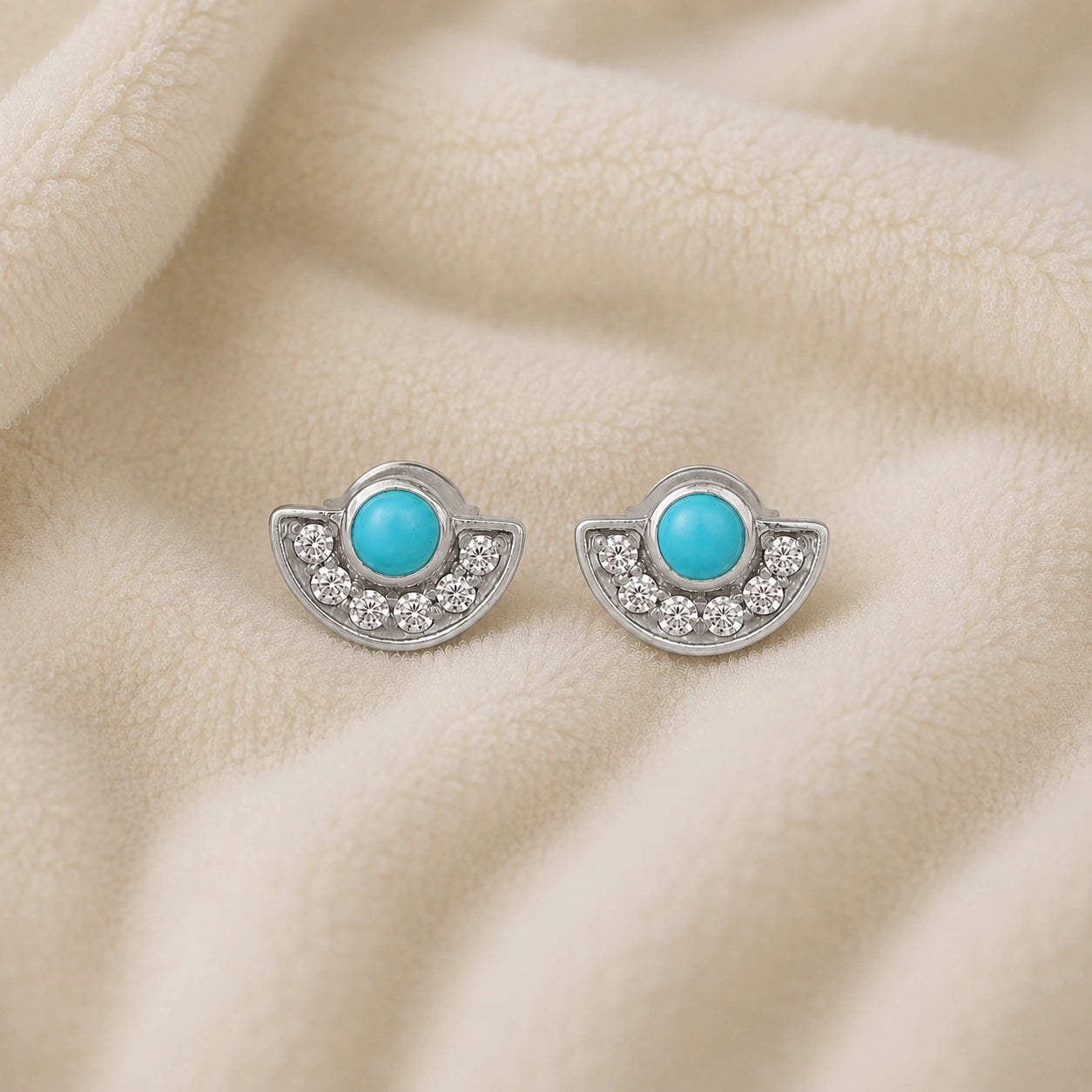Turquoise_earrings_in_sterling_silver_with_turquoise_and_CZ_stones_at_front_angle_view_on_soft_fabric_background