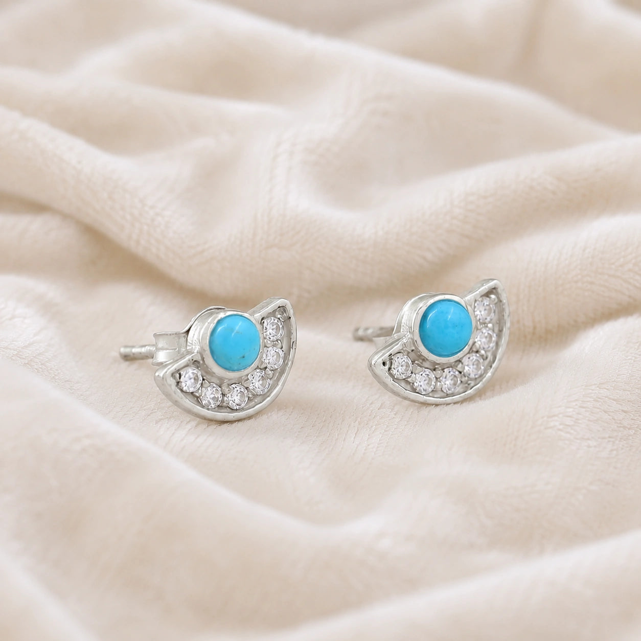 Turquoise_earrings_in_sterling_silver_with_turquoise_and_CZ_stones_at_slight_angle_view_on_soft_fabric_background
