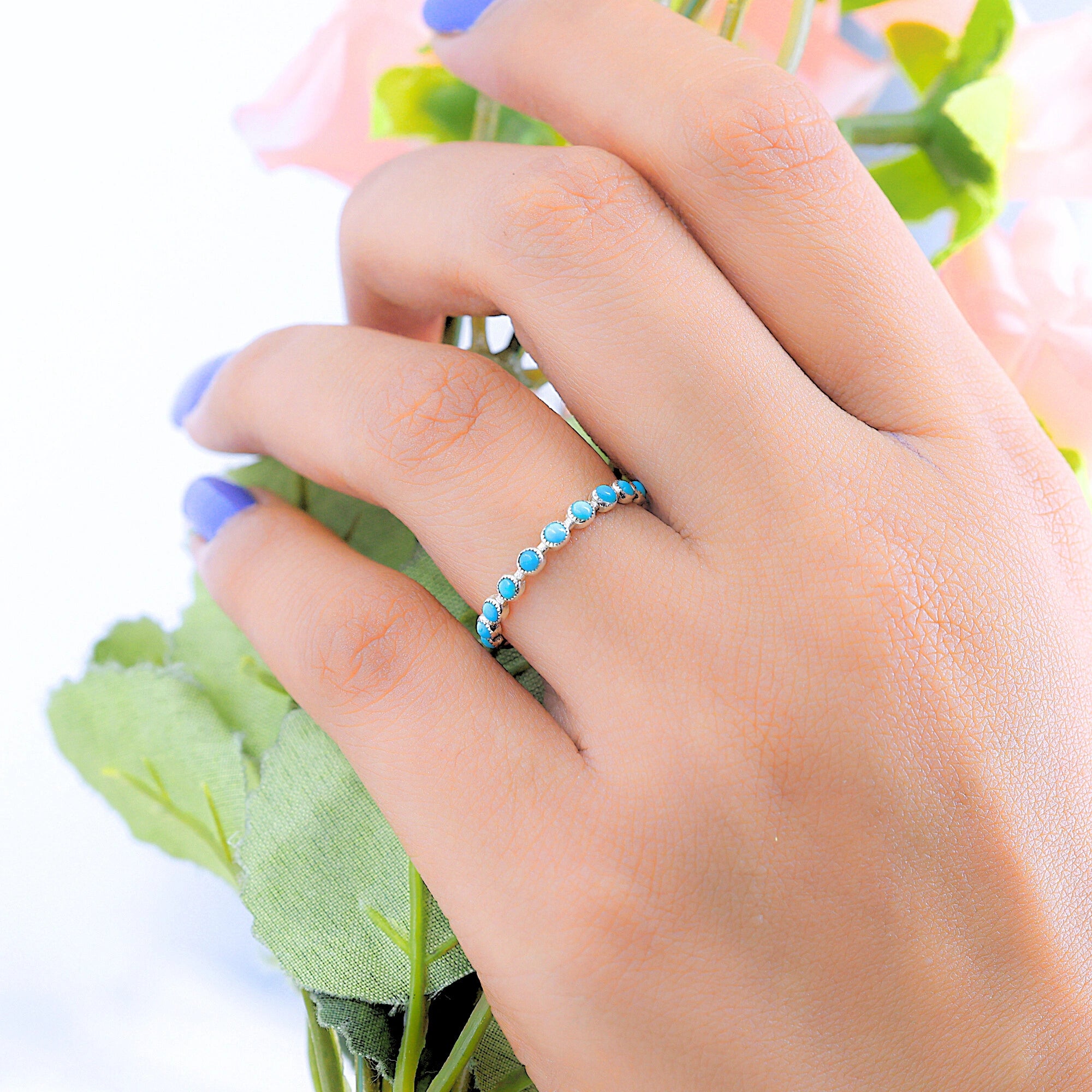 Angled close-up of a sterling silver turquoise ring style gold vermeil eternity band on a hand holding a soft floral element.