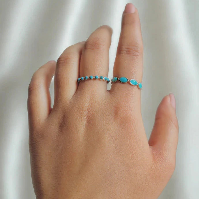 Silver eternity ring with marquise cut turquoise gemstones bezel set low angle view on a white velvet fabric background