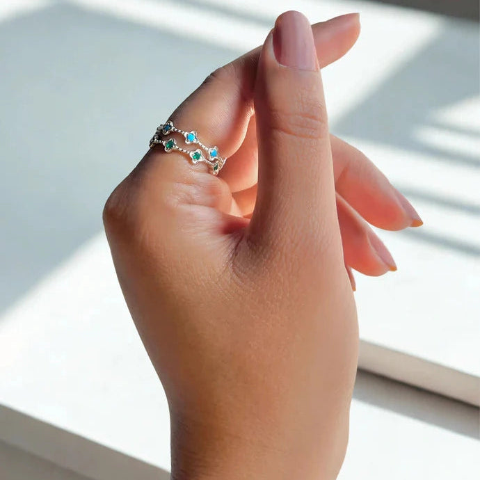 Two eternity band rings sterling silver floral design one green onyx one blue topaz on a woman's finger angled left close up.
