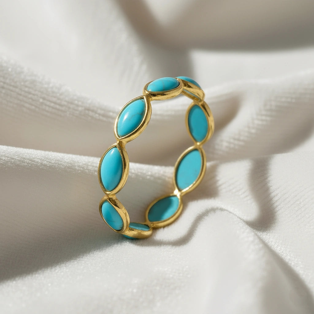 Gold plated silver eternity ring with marquise cut turquoise gemstones elevated view on soft white velvet folded fabric background