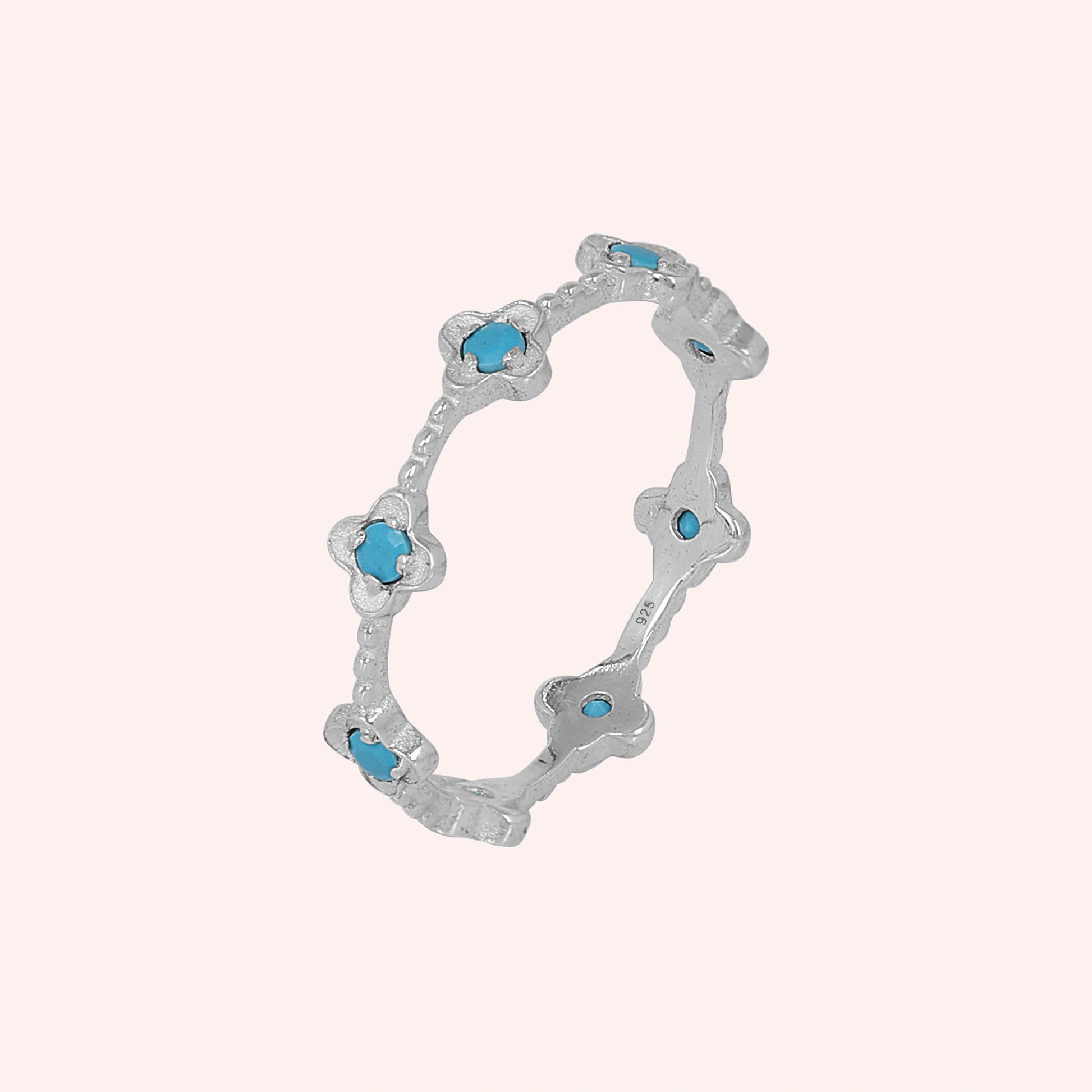 Delicate sterling silver turquoise flower ring featuring clover shapes against a simple light pink background angled view.