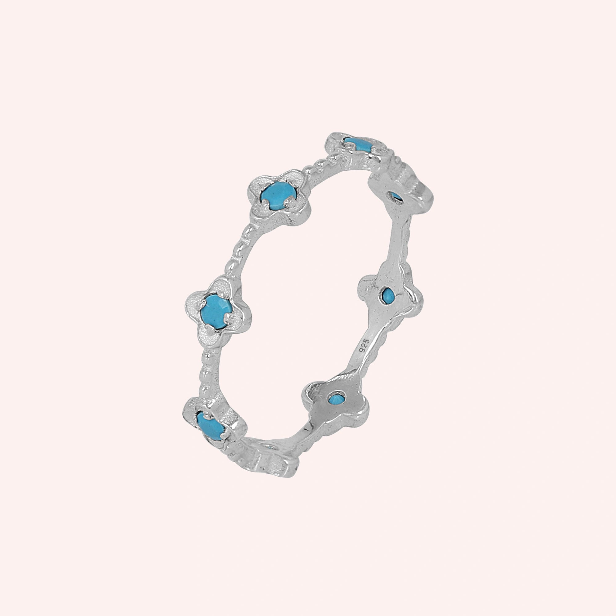 Delicate sterling silver turquoise flower ring featuring clover shapes against a simple light pink background angled view.