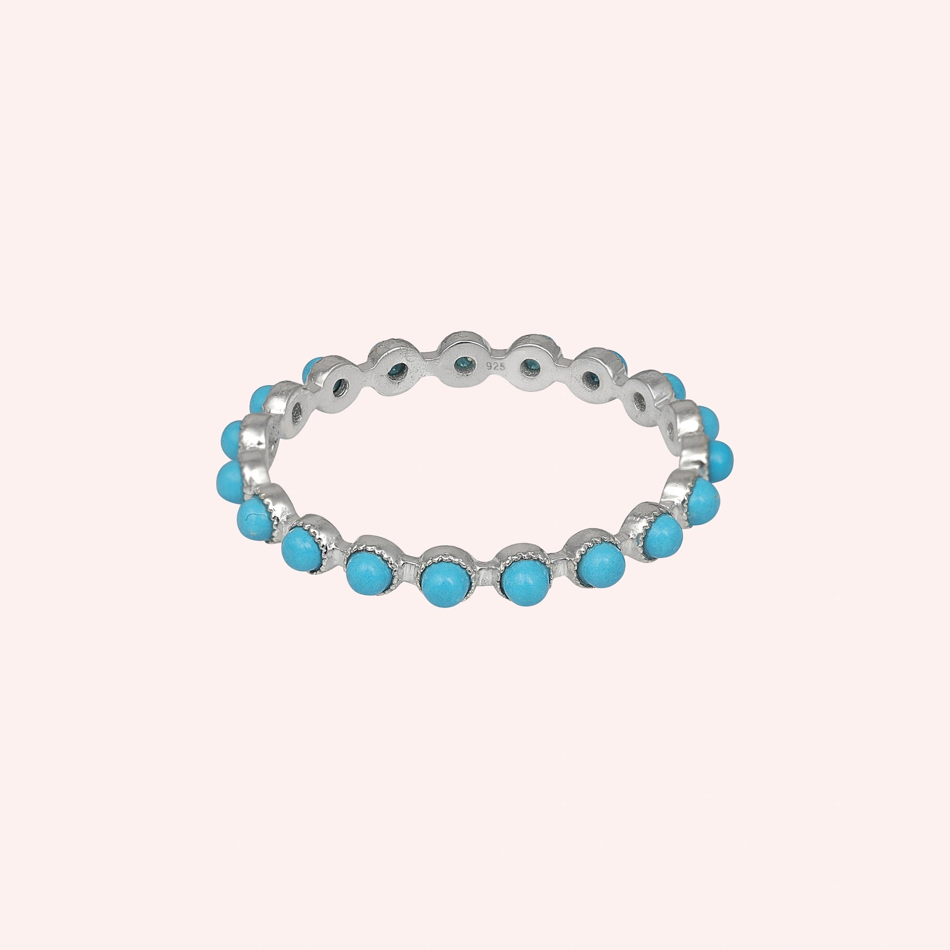 Angled sterling silver turquoise ring a full eternity band featuring round blue turquoise stones on a soft light pink background.