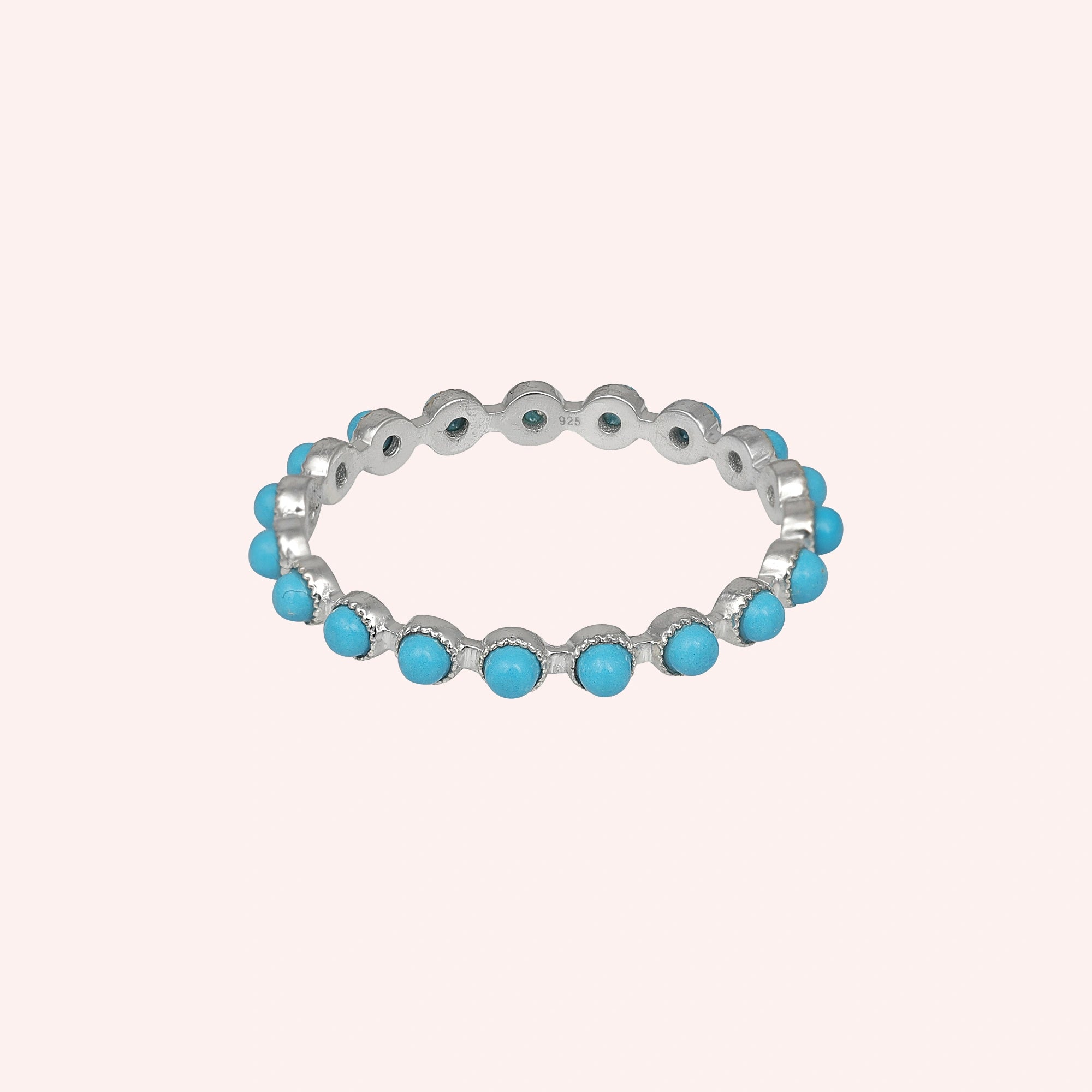 Angled sterling silver turquoise ring a full eternity band featuring round blue turquoise stones on a soft light pink background.