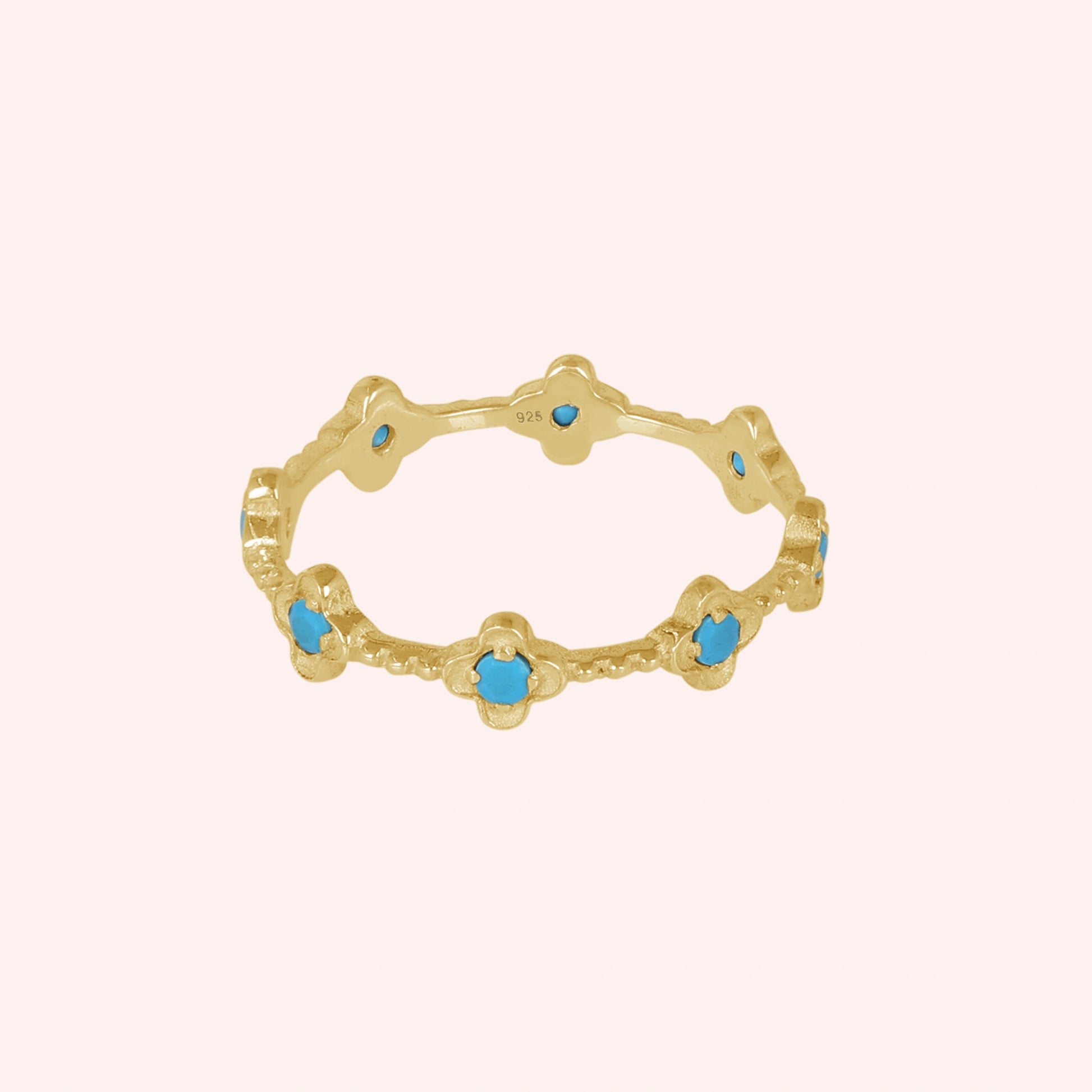 Gold plated flower ring with turquoise gemstones showing detailed craftsmanship against a soft pink background angled view.