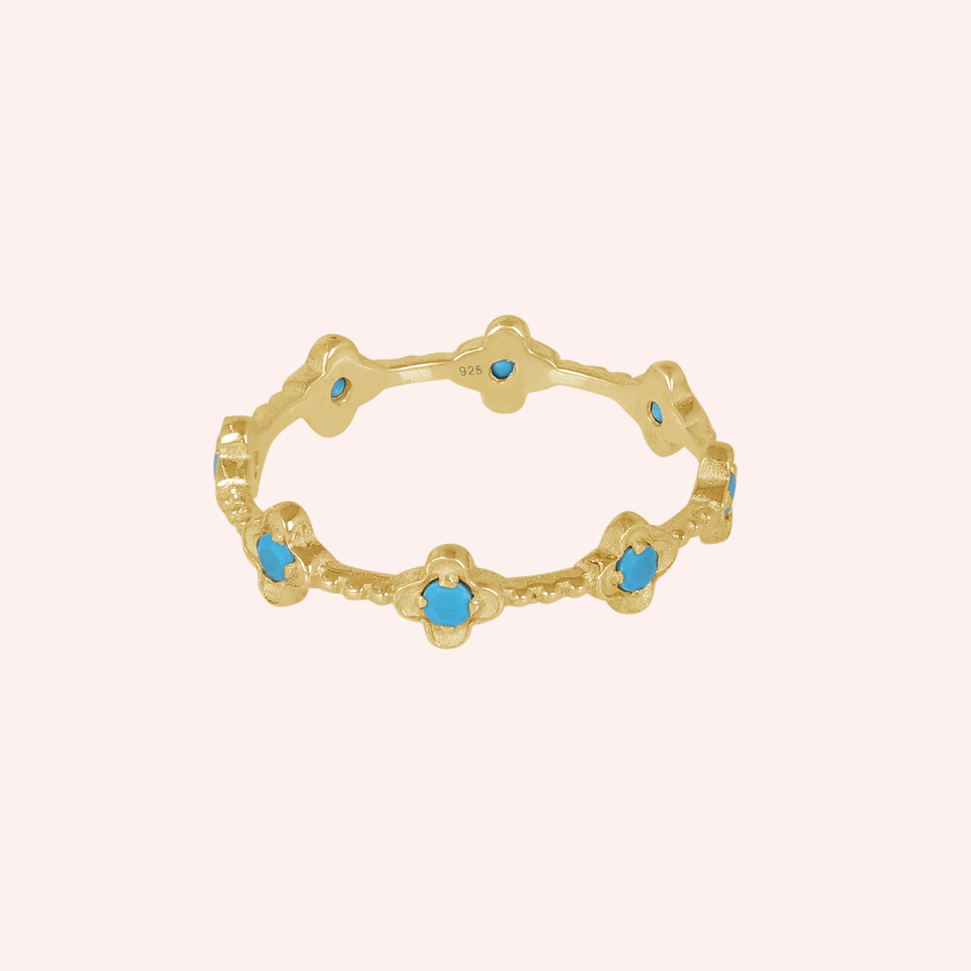 Gold plated flower ring with turquoise gemstones showing detailed craftsmanship against a soft pink background angled view.
