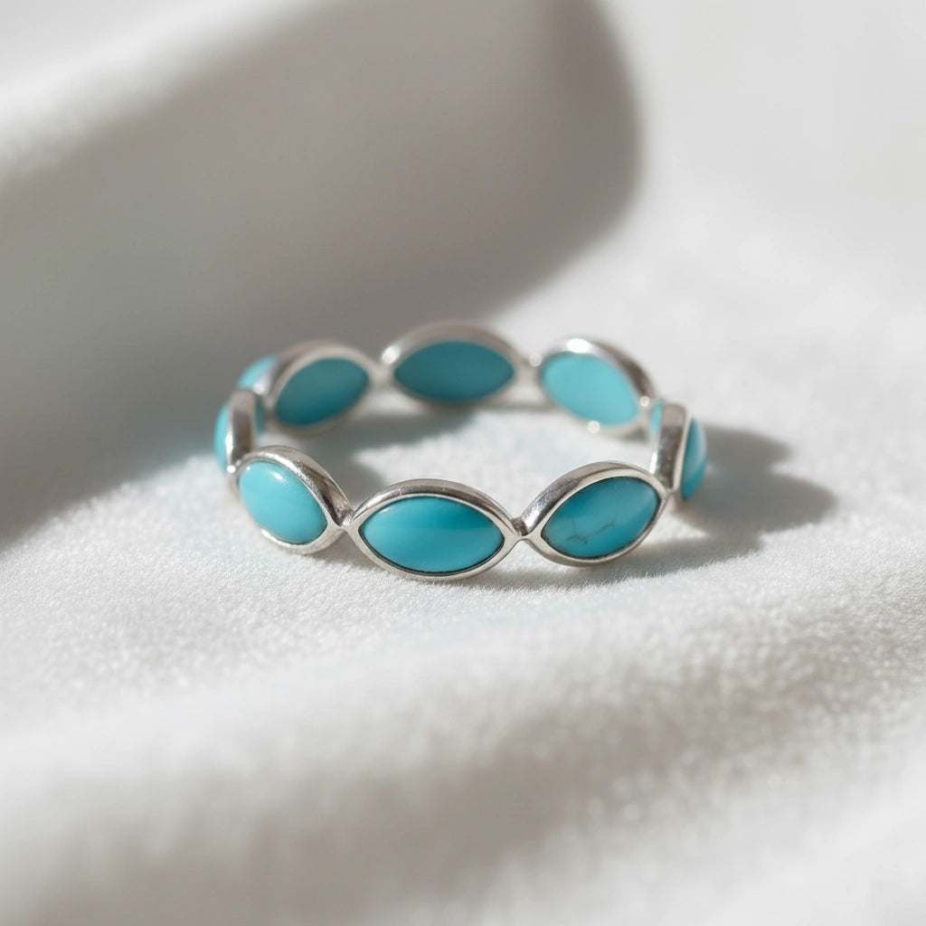 Silver eternity ring with marquise cut turquoise gemstones bezel set low angle view on a white velvet fabric background