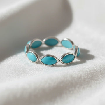 Silver eternity ring with marquise cut turquoise gemstones bezel set low angle view on a white velvet fabric background