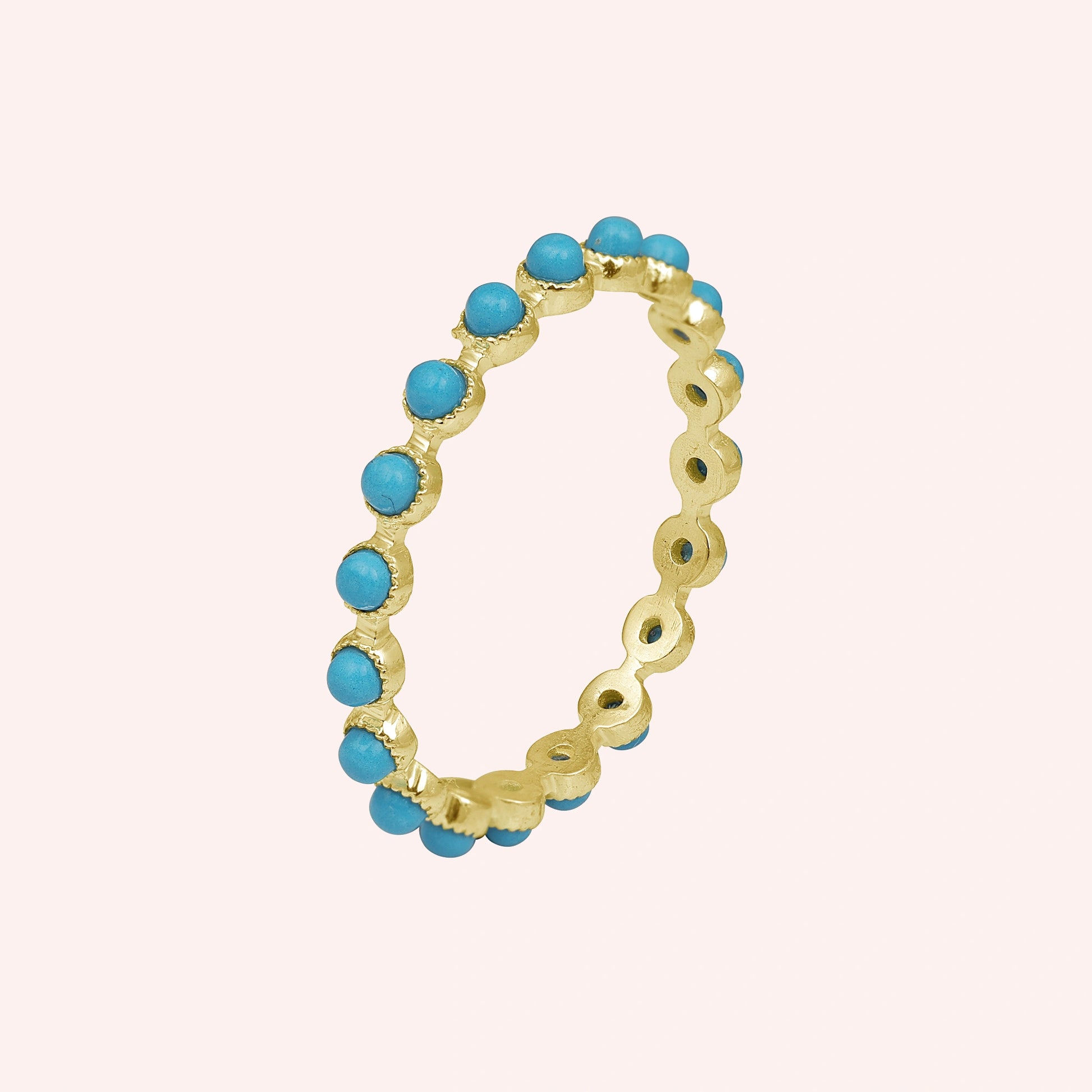 Angled sterling silver turquoise ring a full eternity band featuring round blue stones on a soft light pink background.