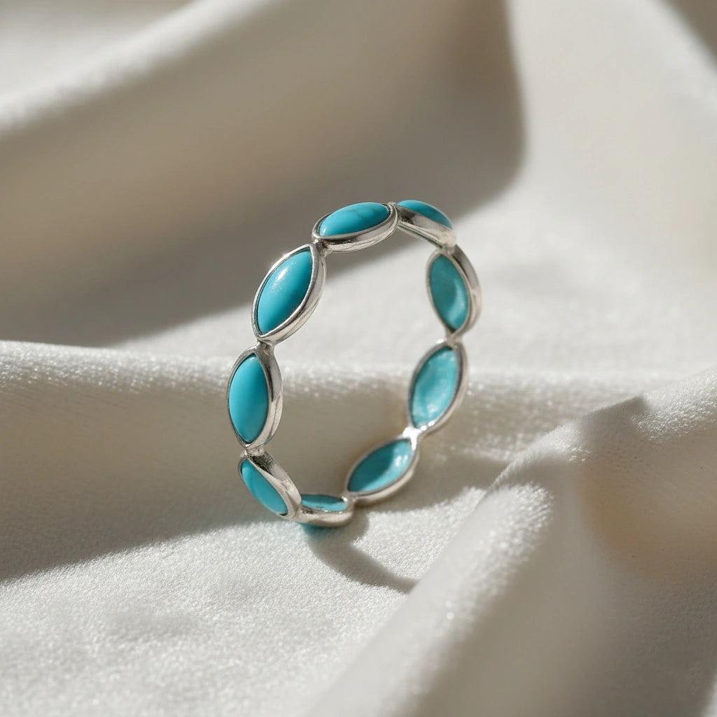 Silver eternity ring with marquise cut turquoise gemstones bezel set elevated view on a white velvet fabric background