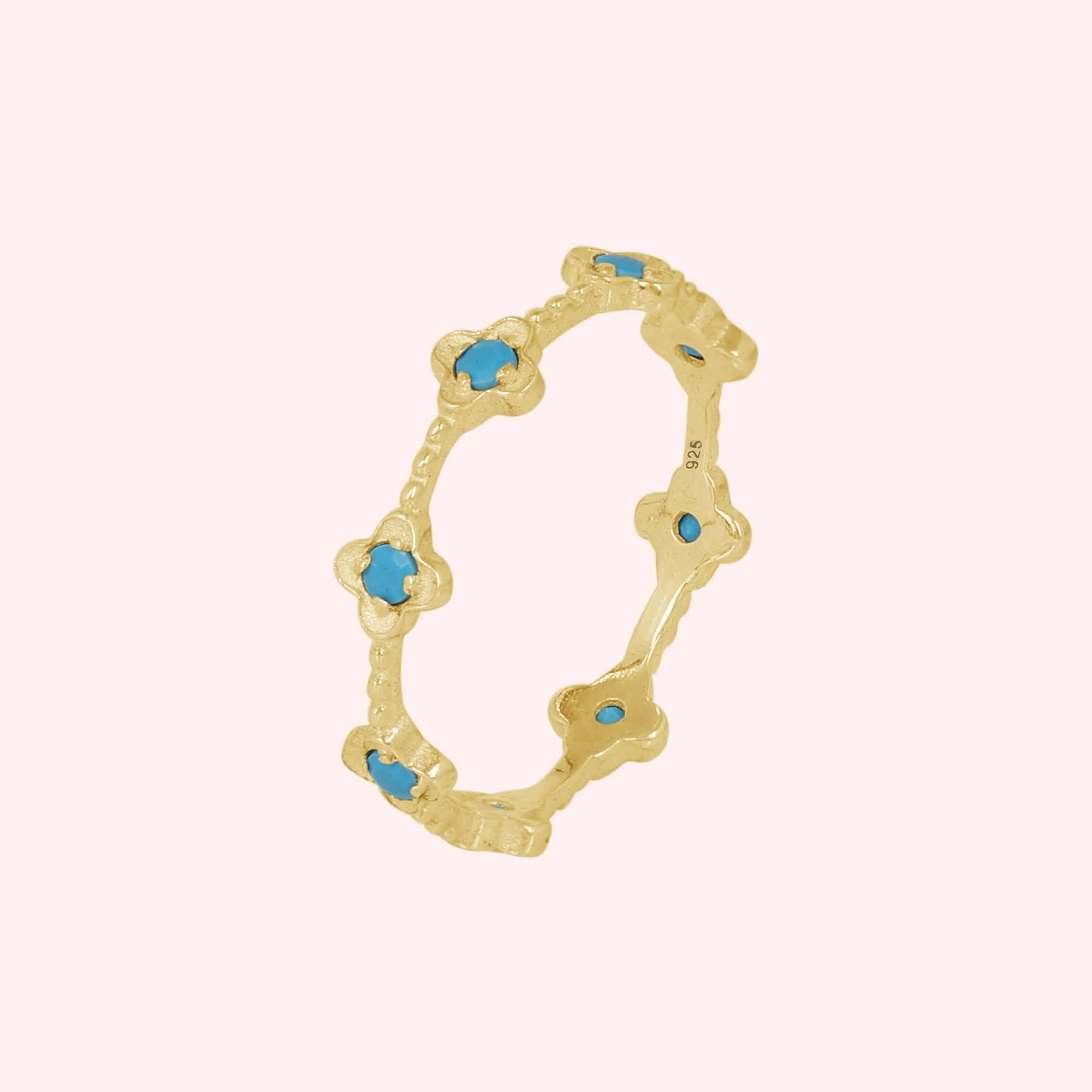 Gold plated flower ring adorned with bright turquoise stones intricate details on a pink background viewed at an angle.
