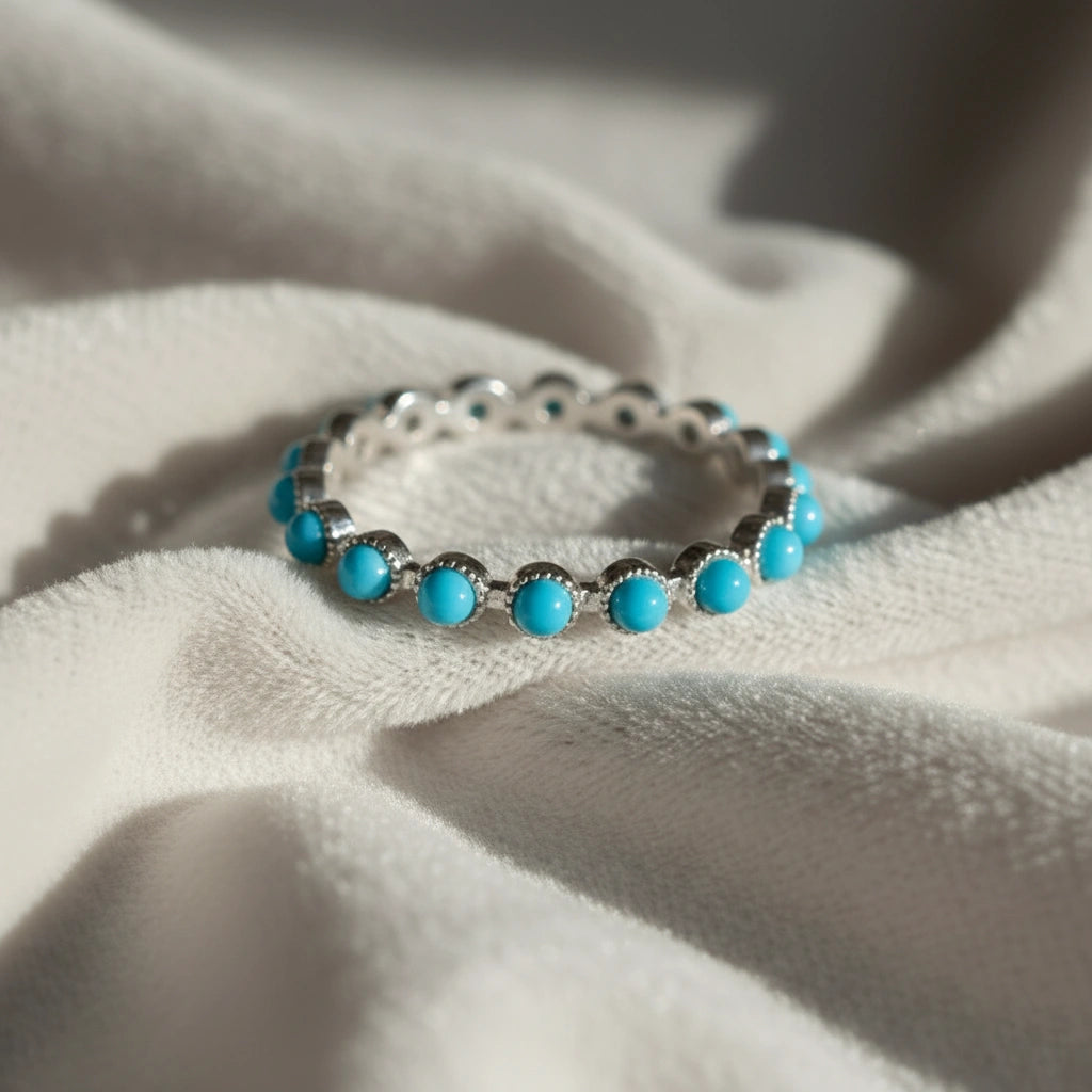 Sterling silver turquoise ring full eternity band angled close-up on soft off-white velvet elegant jewelry piece.