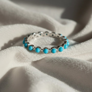 Sterling silver turquoise ring full eternity band angled close-up on soft off-white velvet elegant jewelry piece.