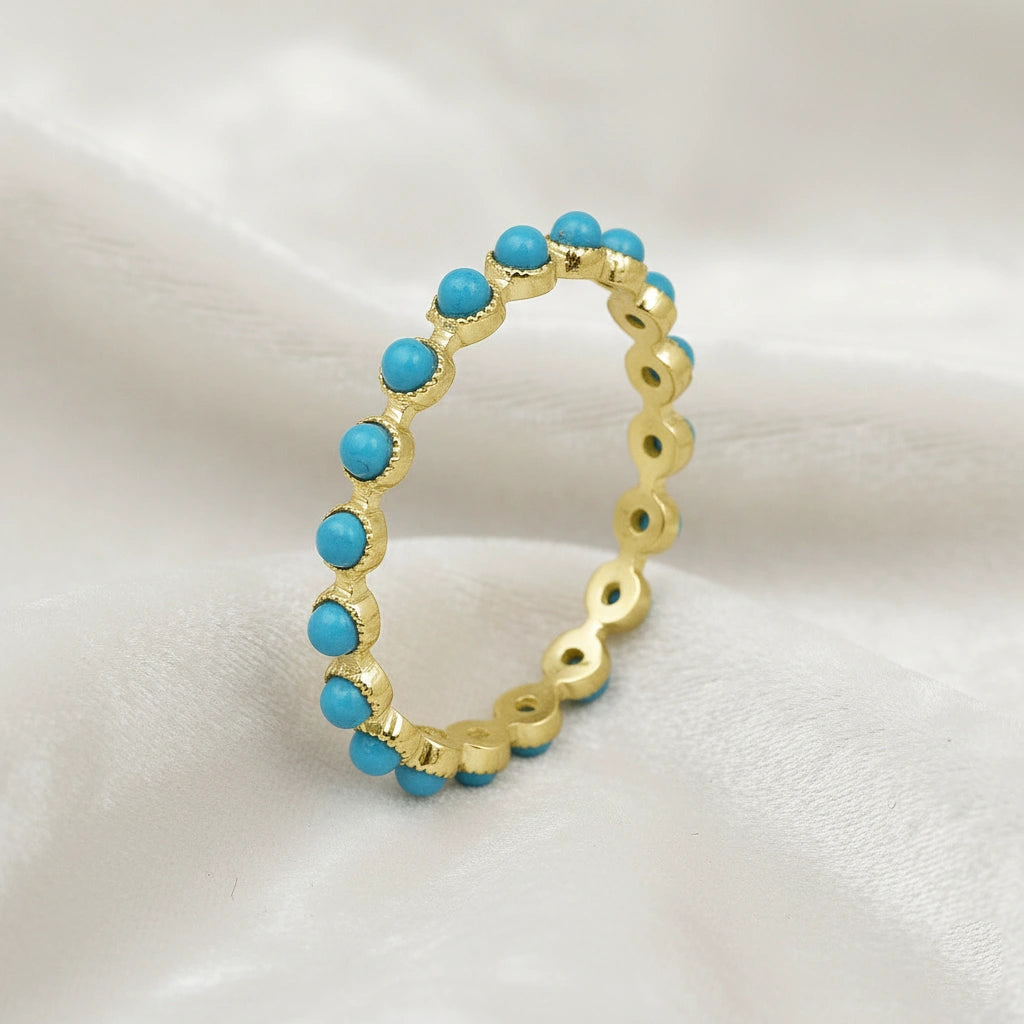 Angled sterling silver turquoise ring style gold vermeil full eternity band with blue round stones on draped white velvet fabric detail.